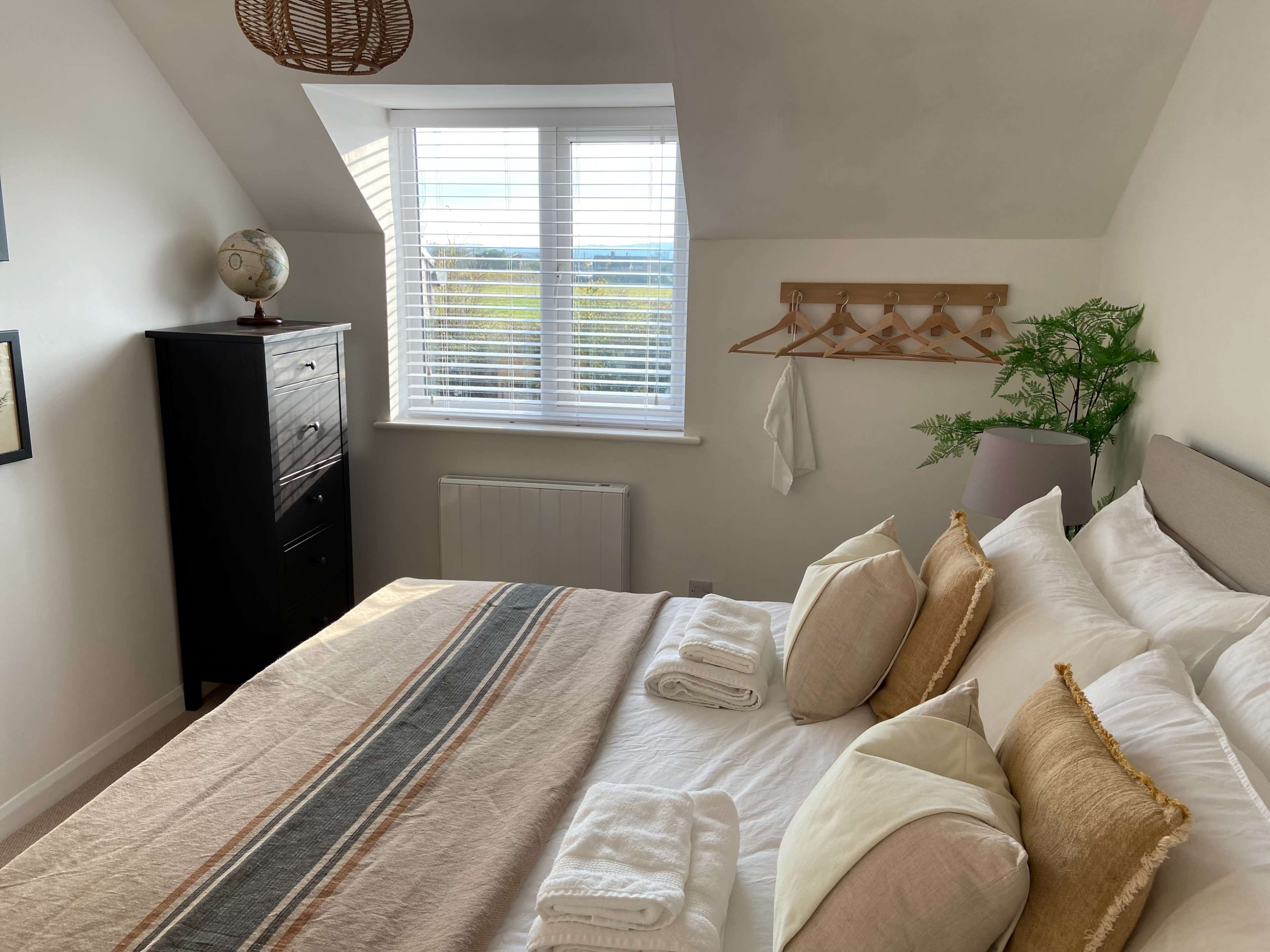 A well-organized bedroom with a double bed, decorative pillows, a black dresser, and a window allowing natural light to enter.