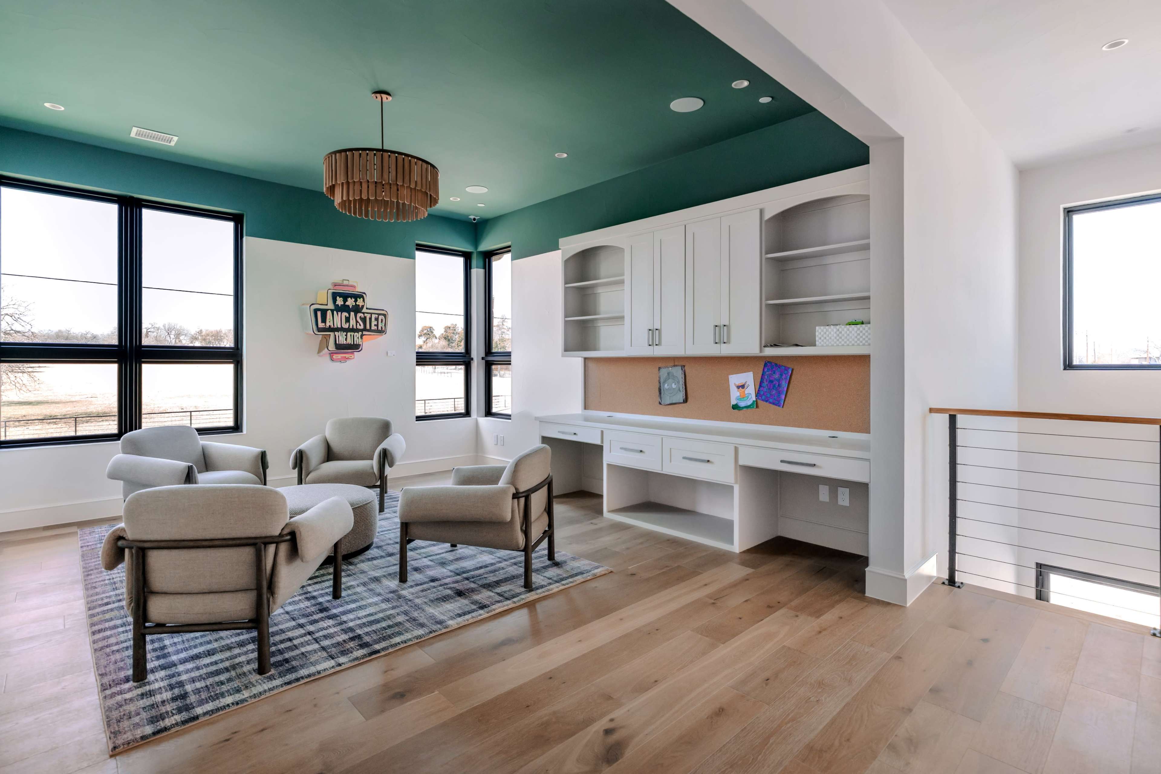 The room features a seating area with four light-colored chairs arranged around a rug, and a built-in desk with shelves along one wall, all under a green ceiling.