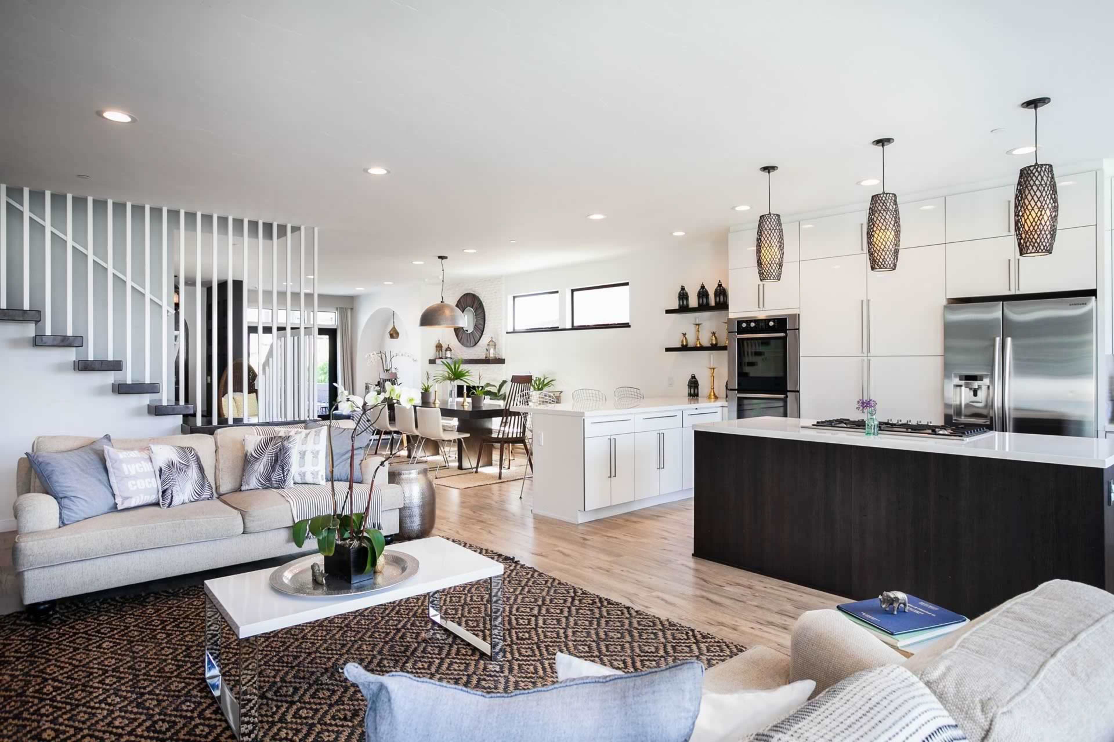 A modern open-concept living space featuring a kitchen with a dark island, a dining area, and a cozy seating arrangement in front of a large window.