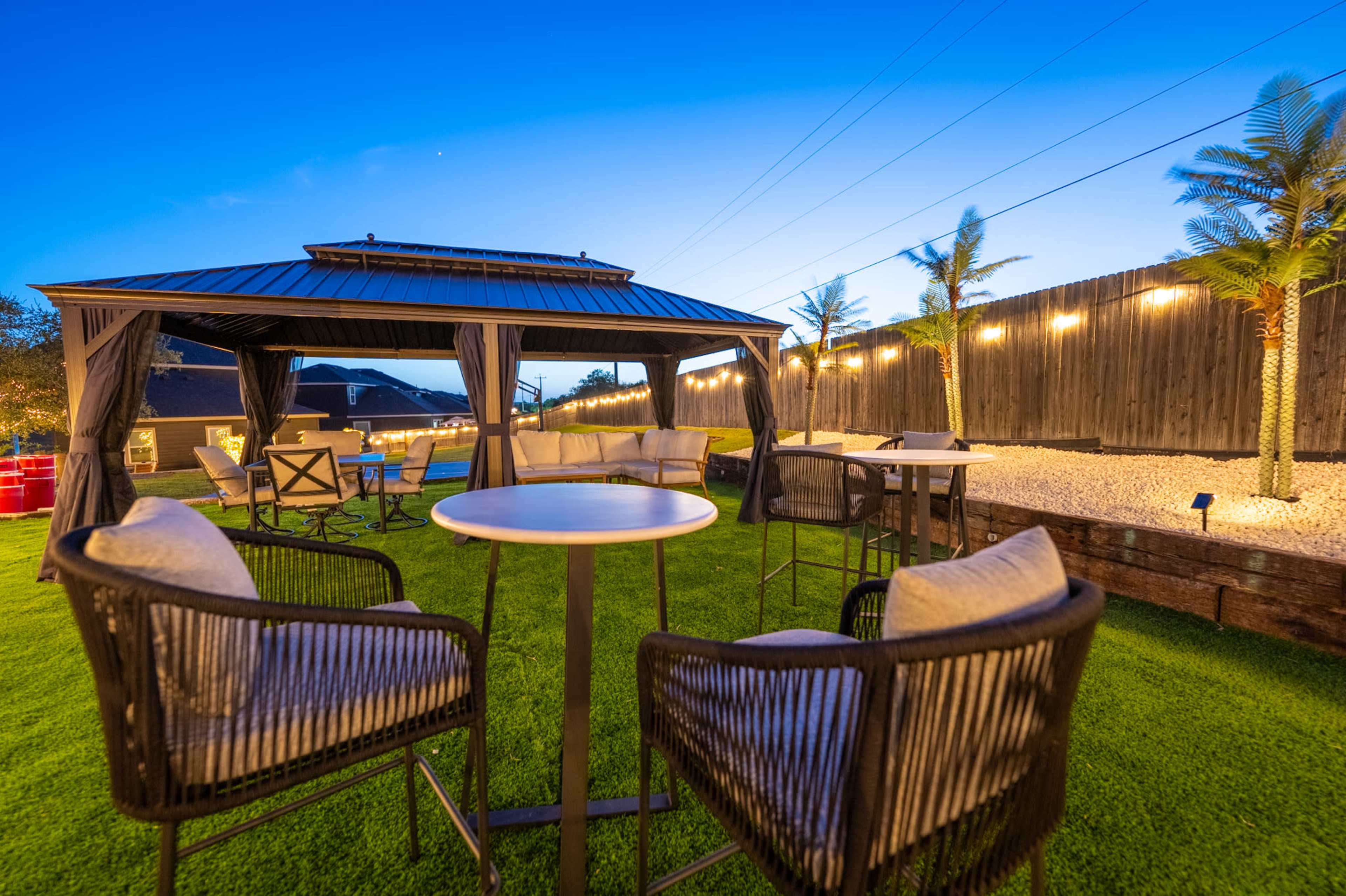 The image shows a backyard with a gazebo, outdoor seating area, and palm trees under a twilight sky.