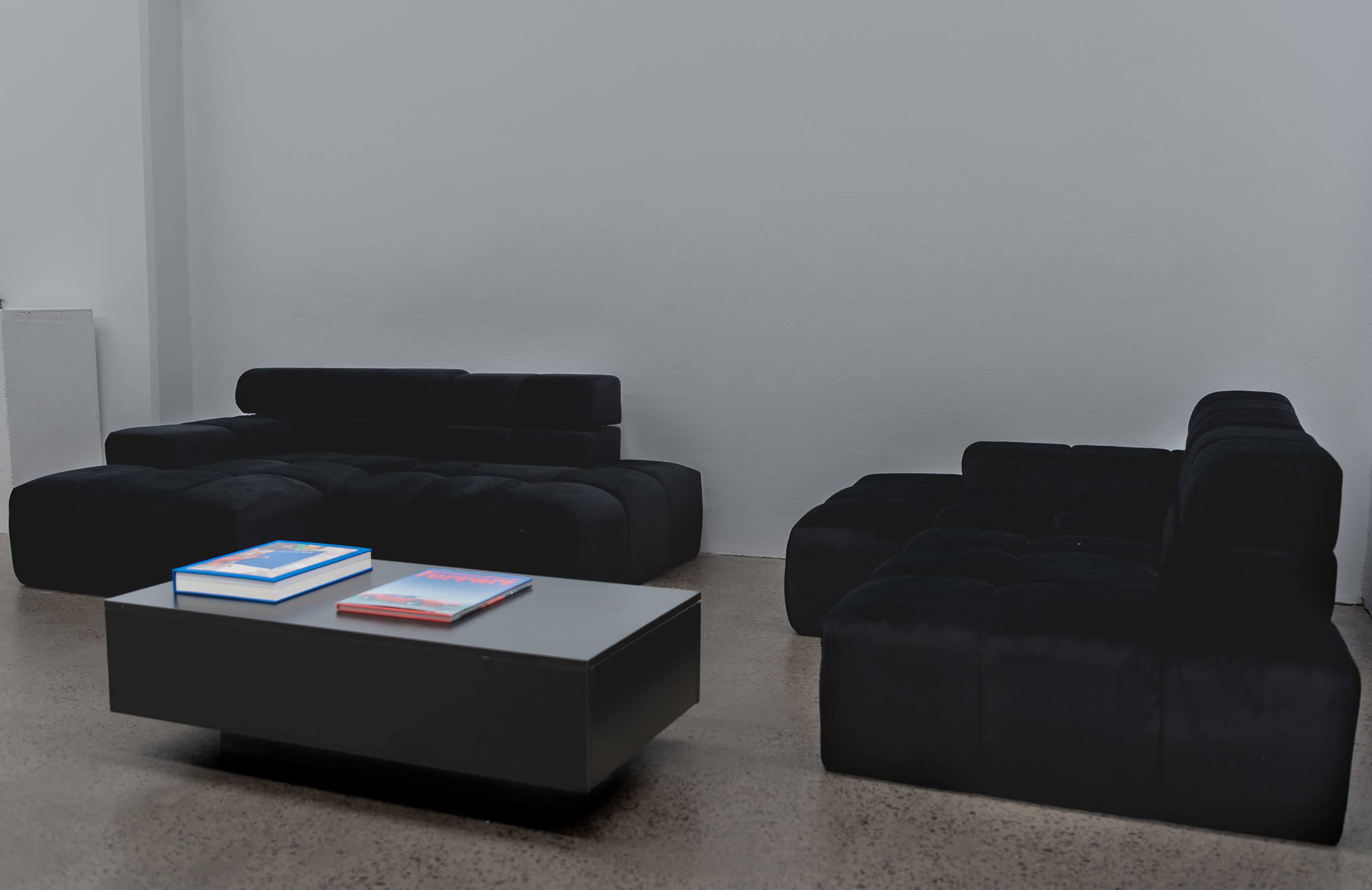 A minimalist lounge area with a black sectional sofa and a low coffee table featuring two stacked books.
