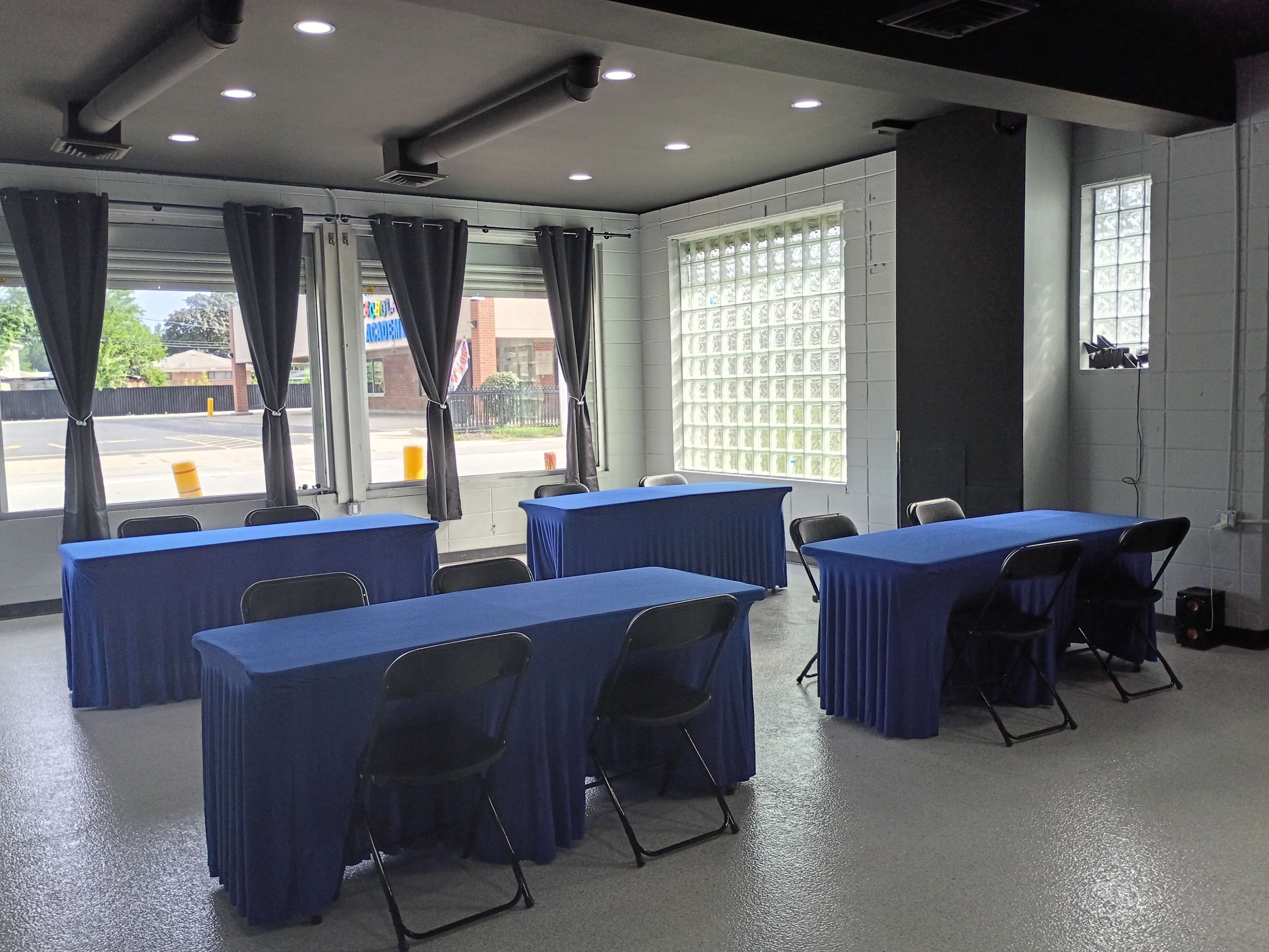 The image shows a well-lit meeting room with several blue-draped tables and black chairs arranged neatly around them.