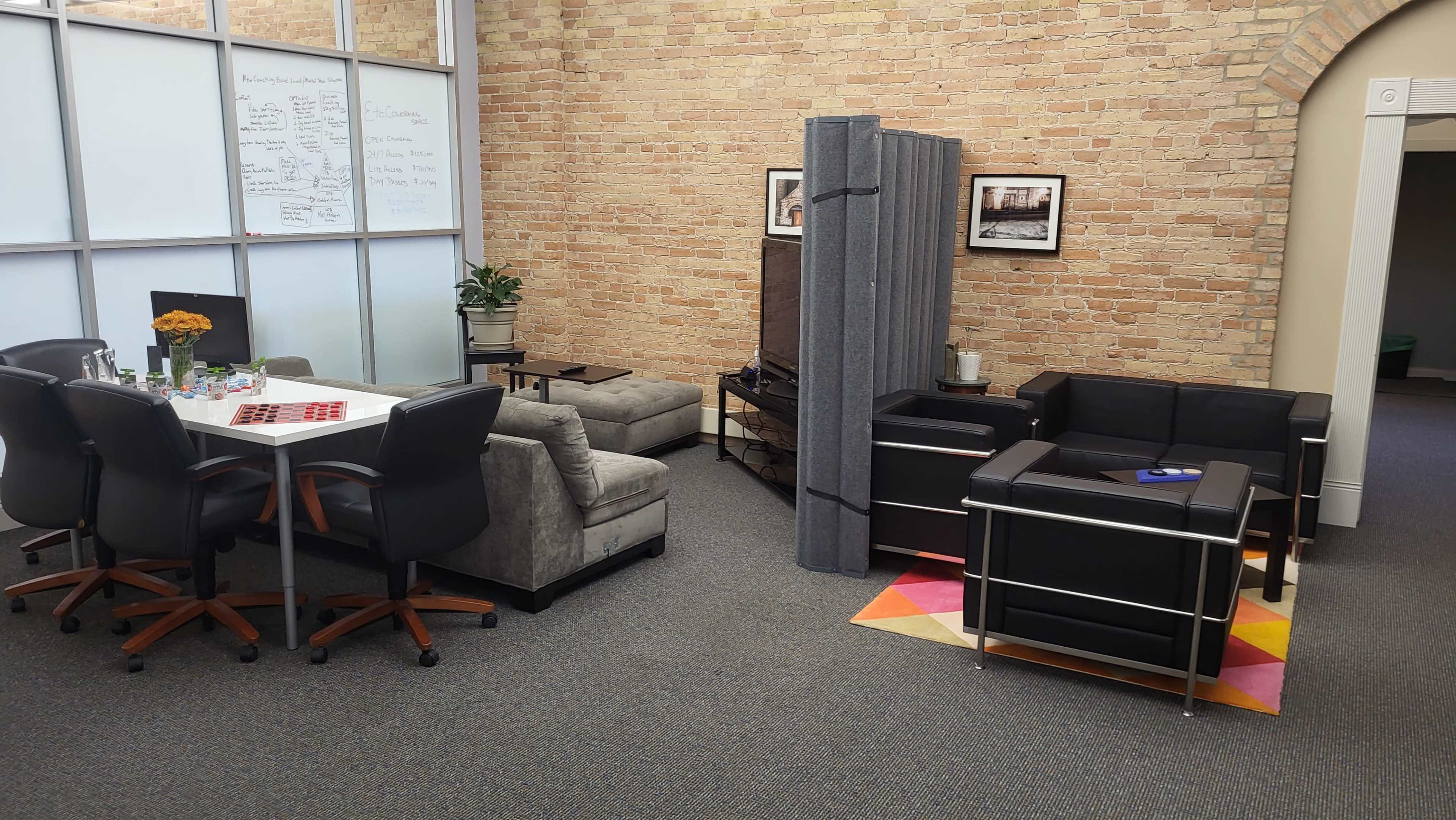 A modern office space with a meeting area featuring a large table and chairs, and a lounge area outfitted with sofas and a privacy screen.