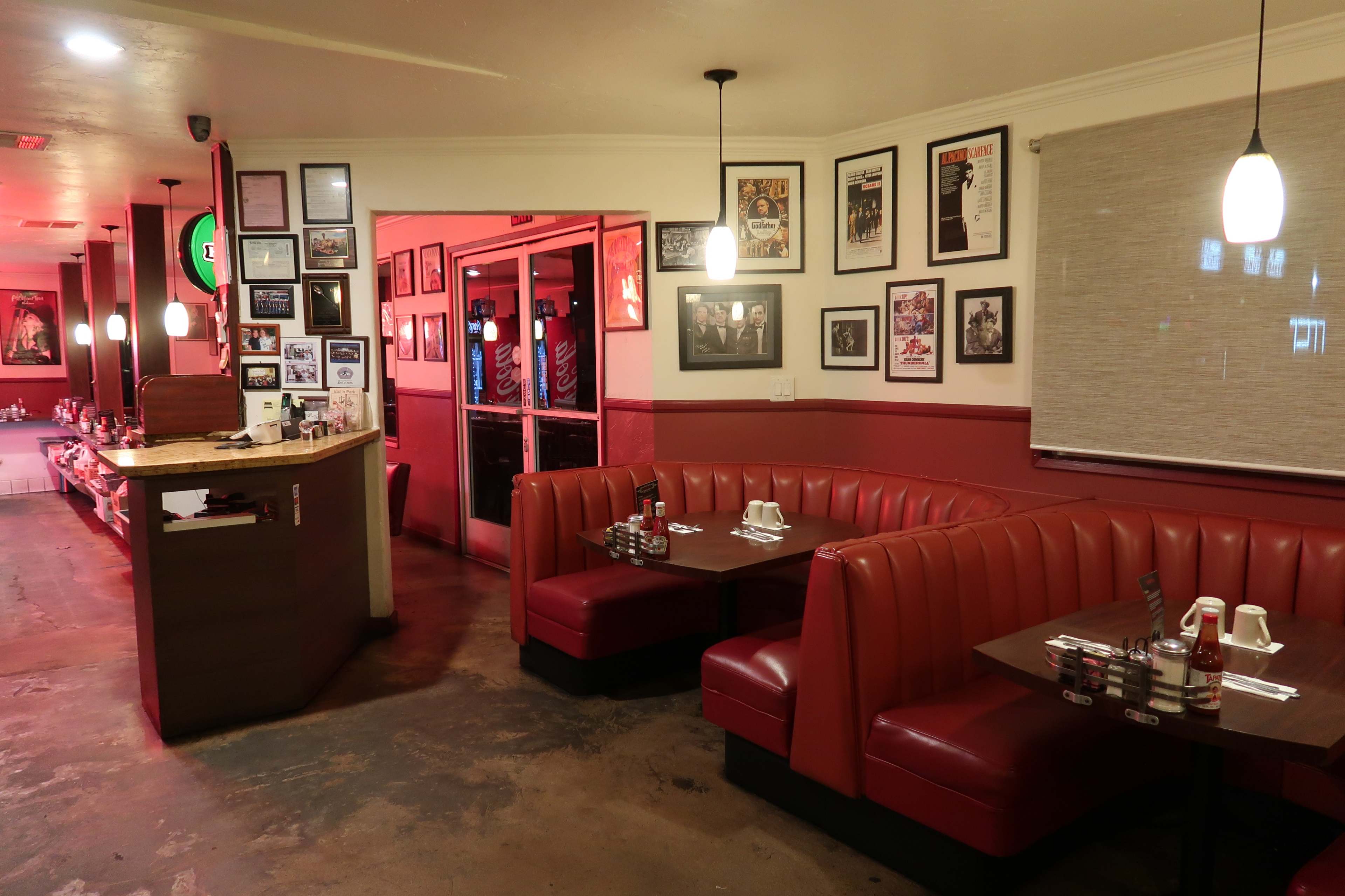 The image shows a diner interior featuring red booths, a food service counter, and walls adorned with framed photographs and posters.