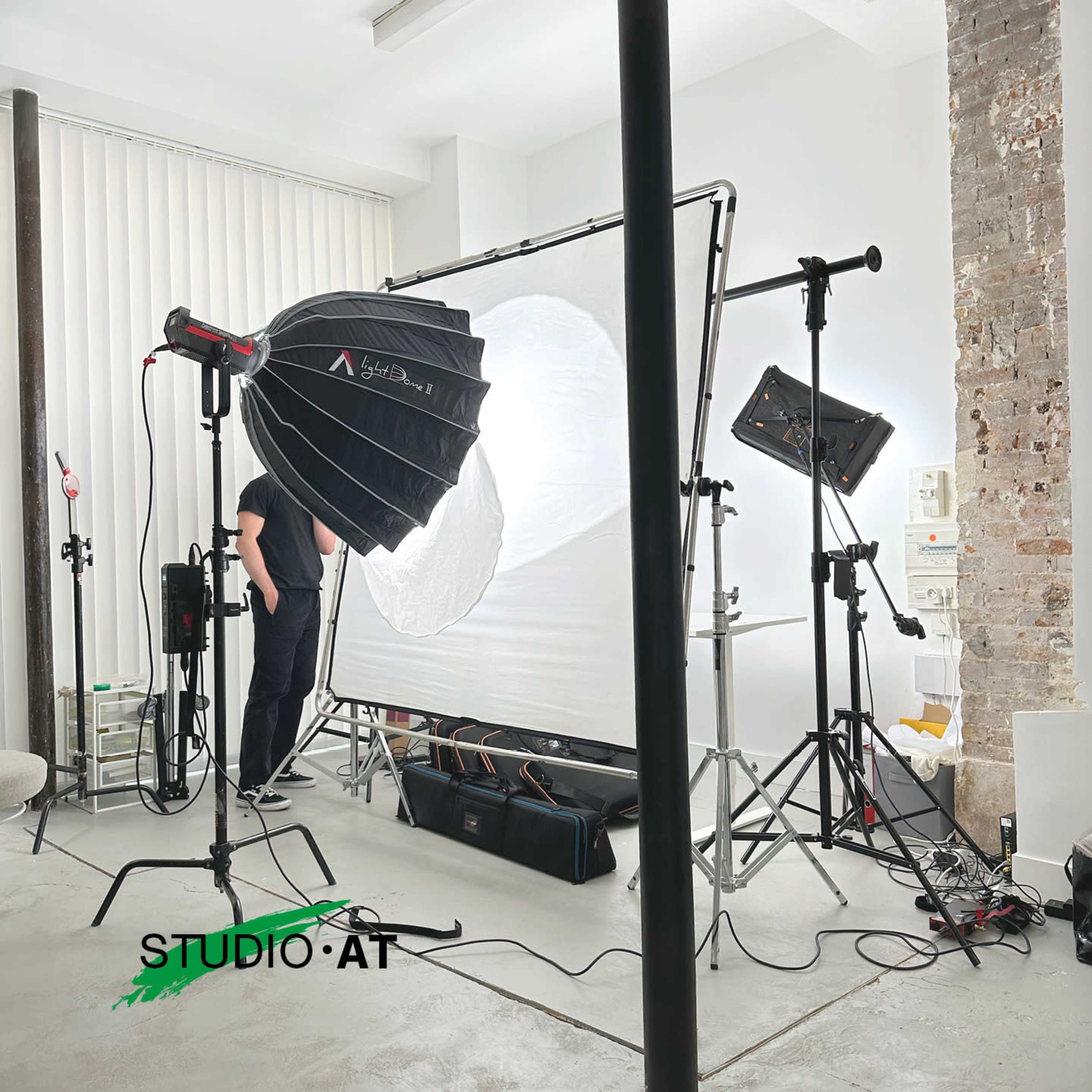 The image shows a well-equipped photography studio with lighting equipment, reflectors, and a backdrop setup.