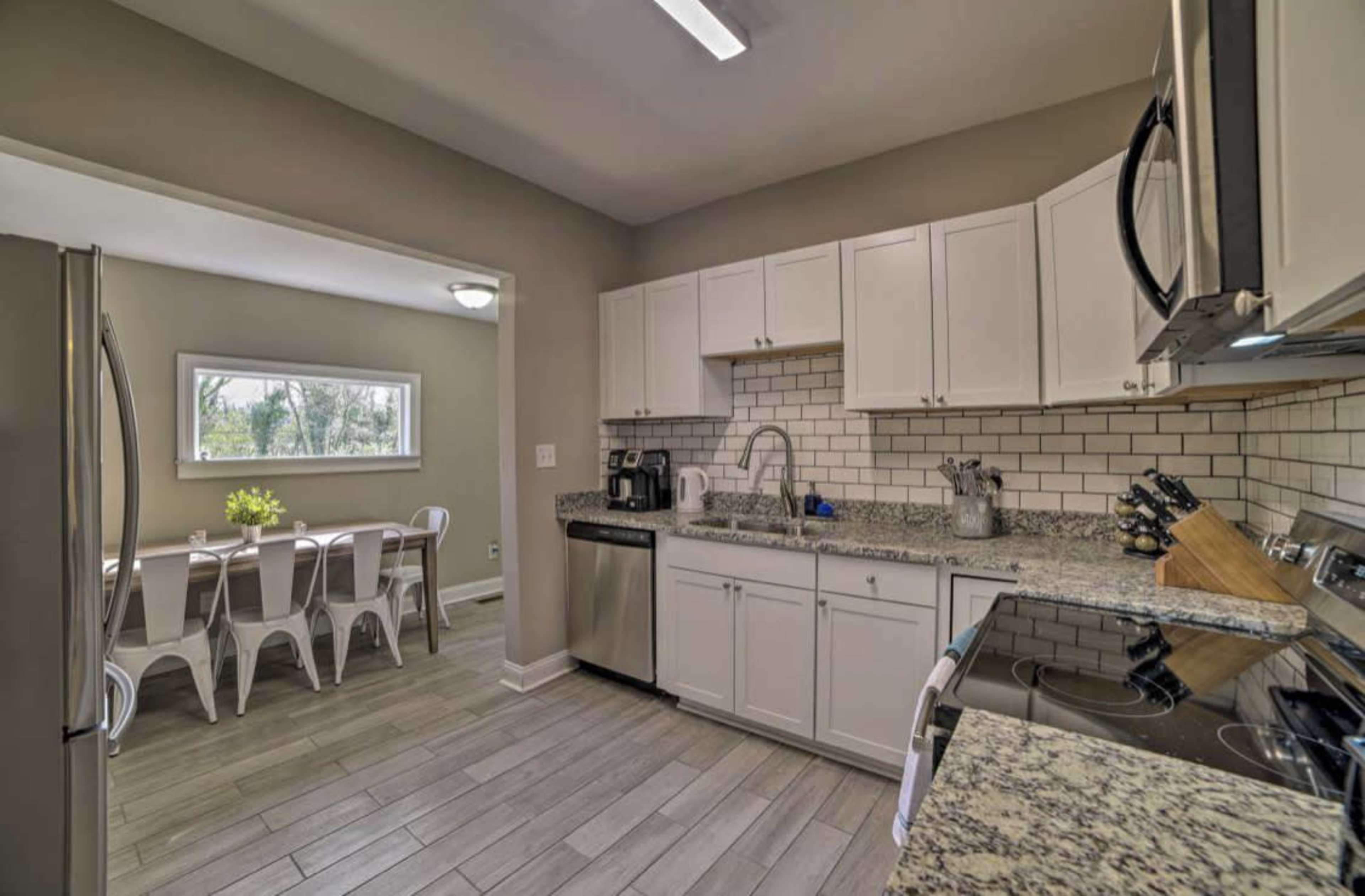 A modern kitchen features white cabinets, granite countertops, stainless steel appliances, and a view into an adjacent dining area with a table and chairs.