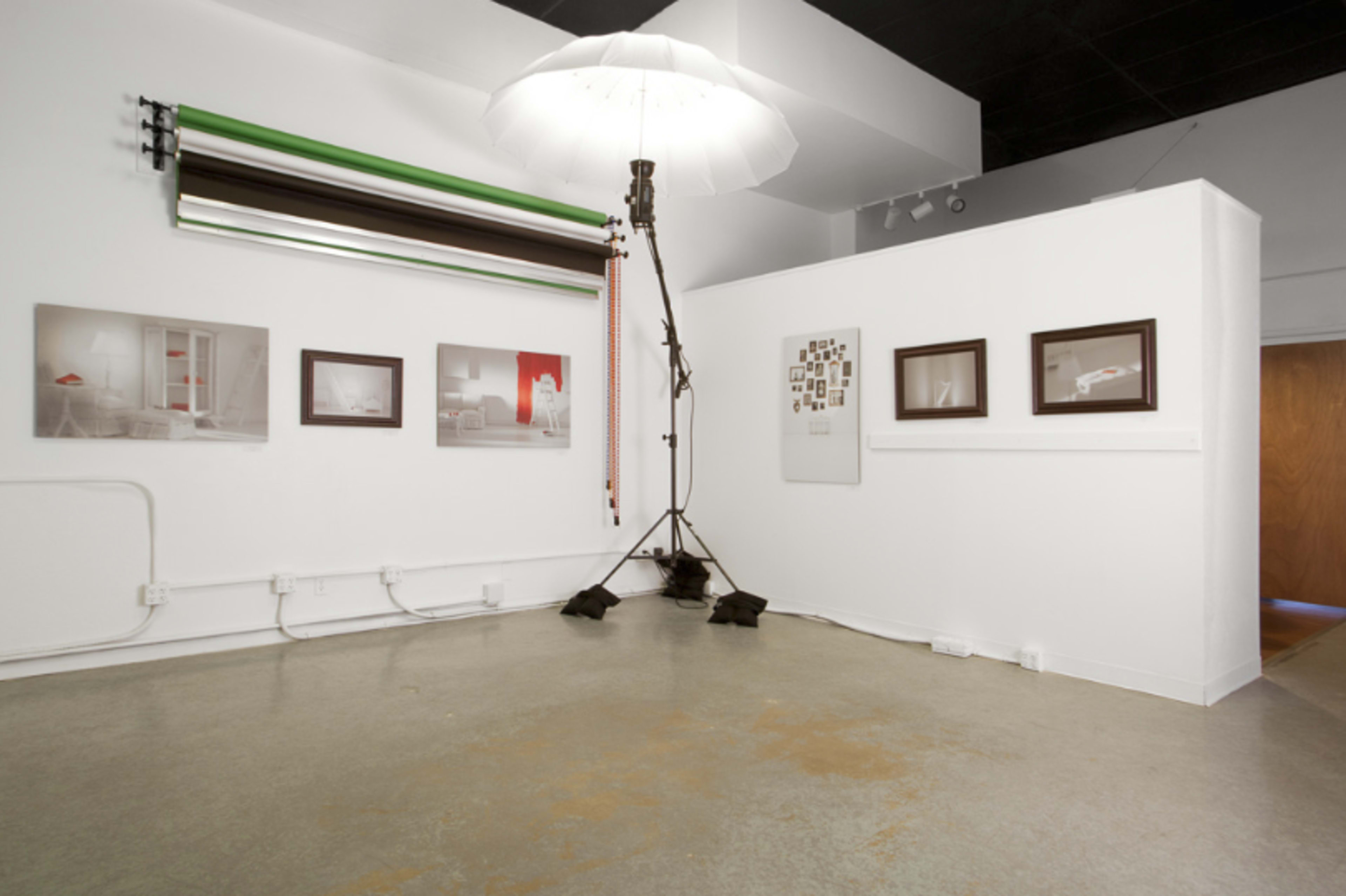 A minimalist photography studio with a backdrop setup, framed photographs on the walls, and a large umbrella light in the center.
