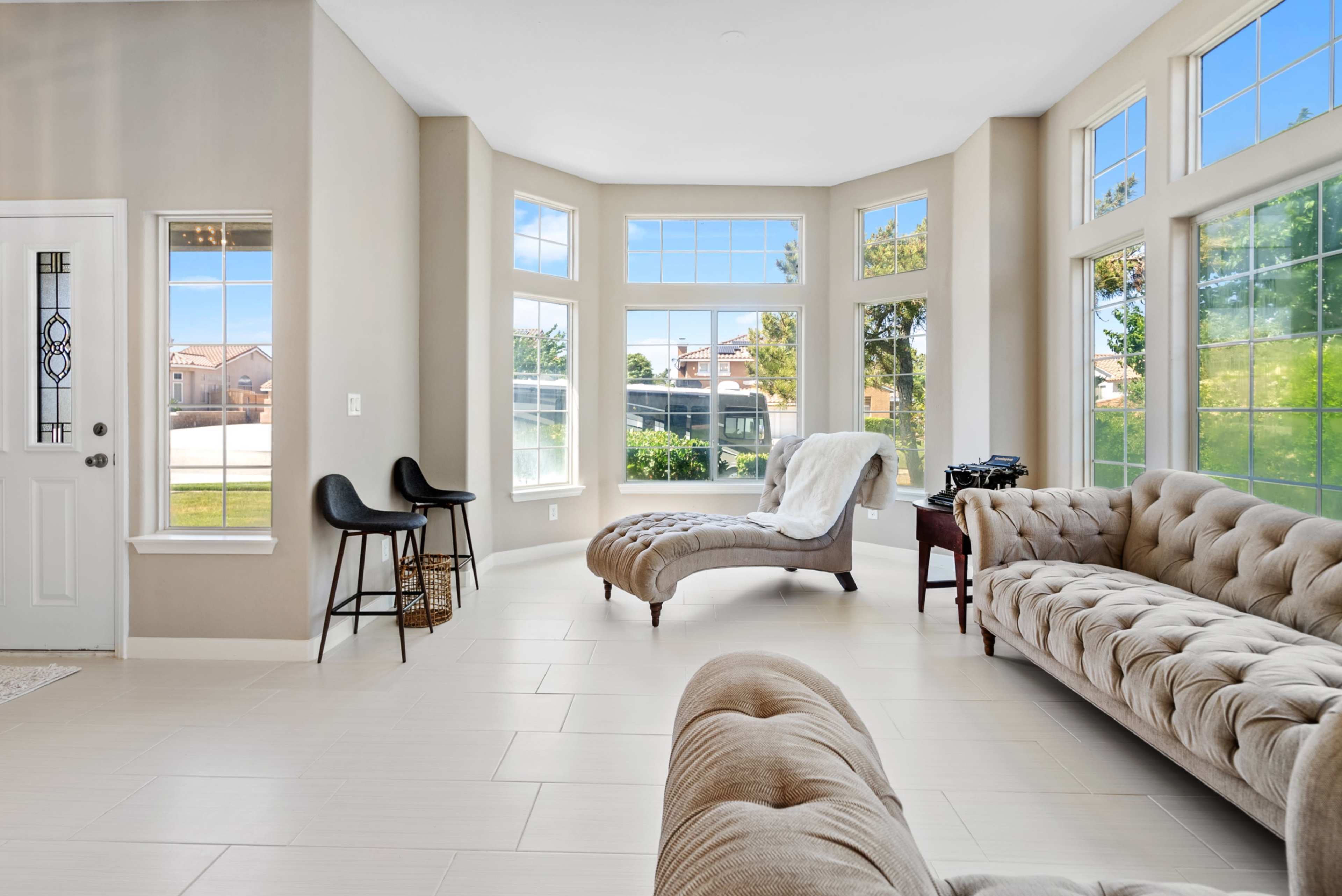 A bright living room features large windows, modern furniture, and a cozy seating area.