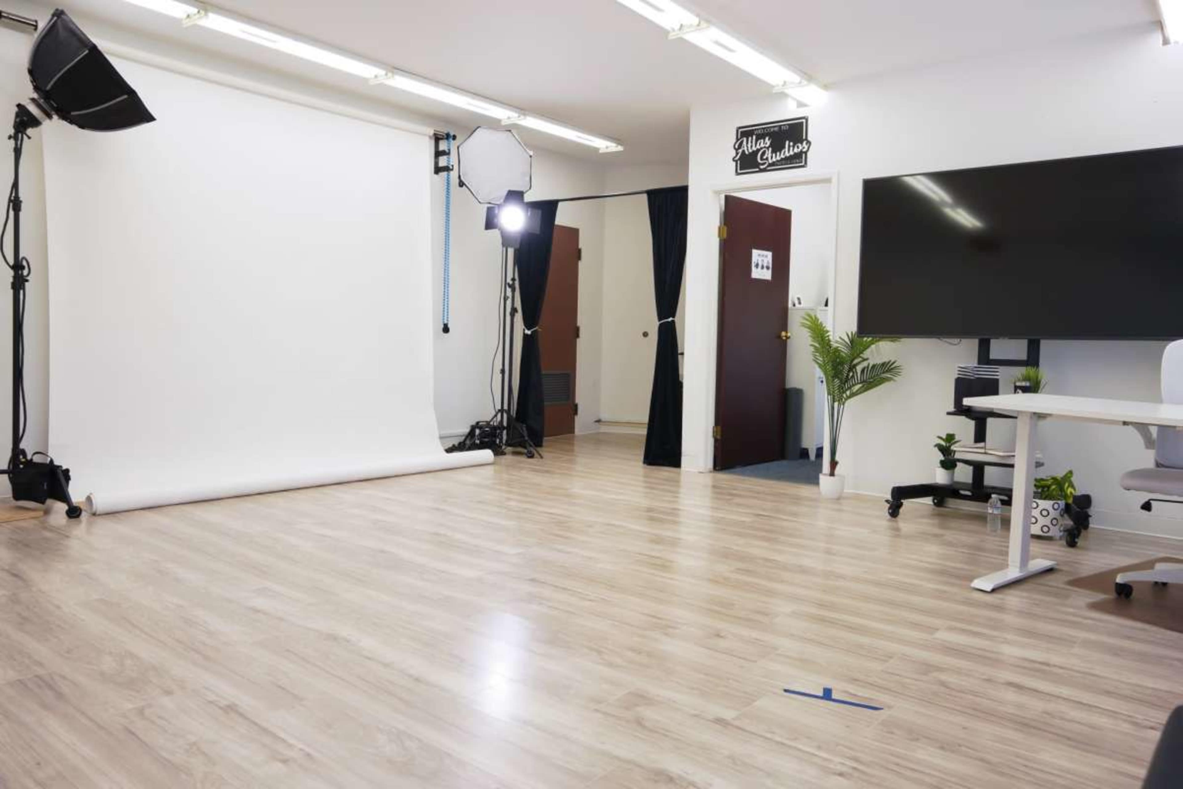 A well-lit photography studio featuring a white backdrop, studio lights, and a workspace with a desk and chair.