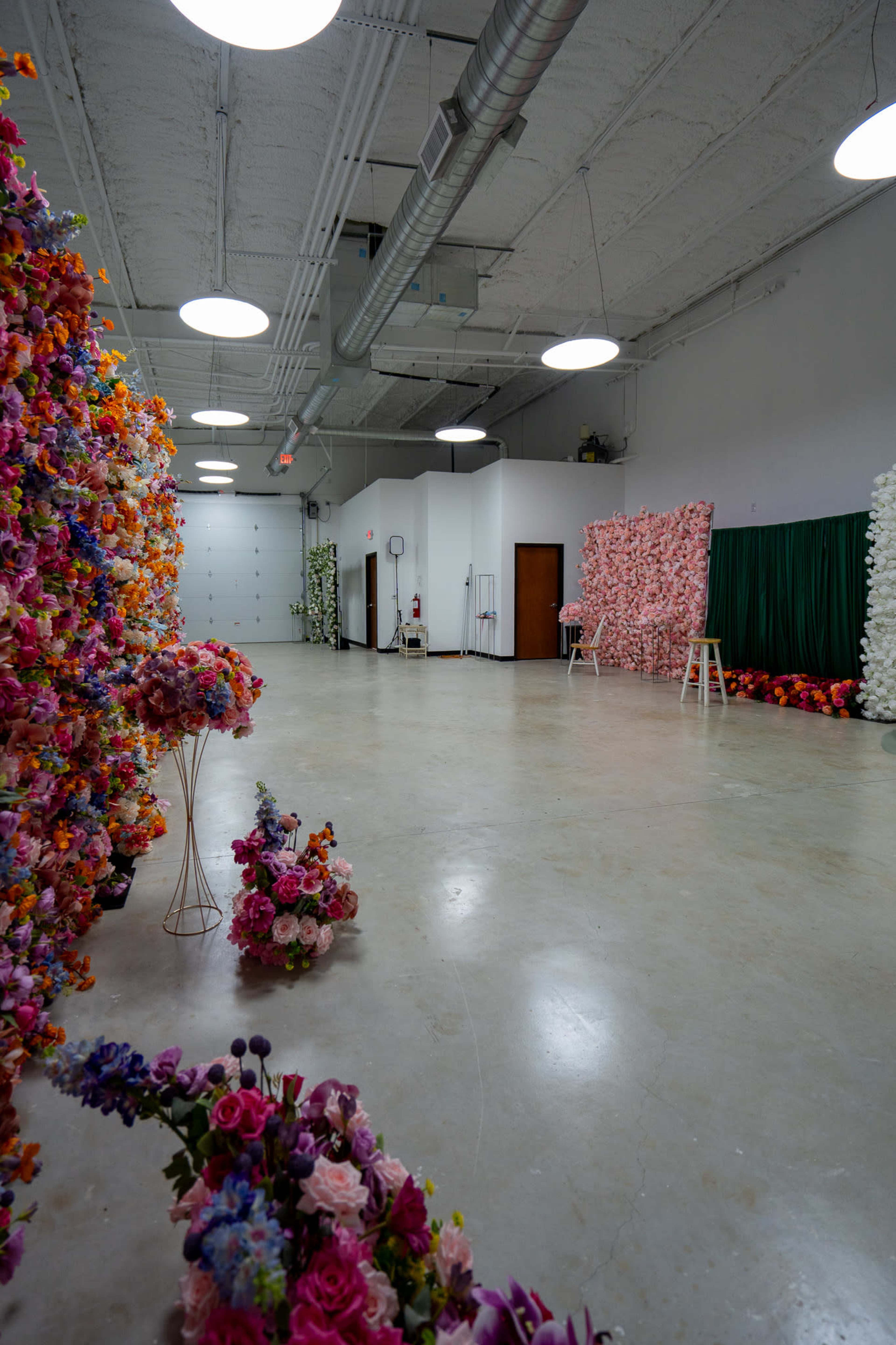 The image shows a spacious interior with flower walls made of various artificial blooms arranged in clusters, along with scattered floral arrangements on the floor.