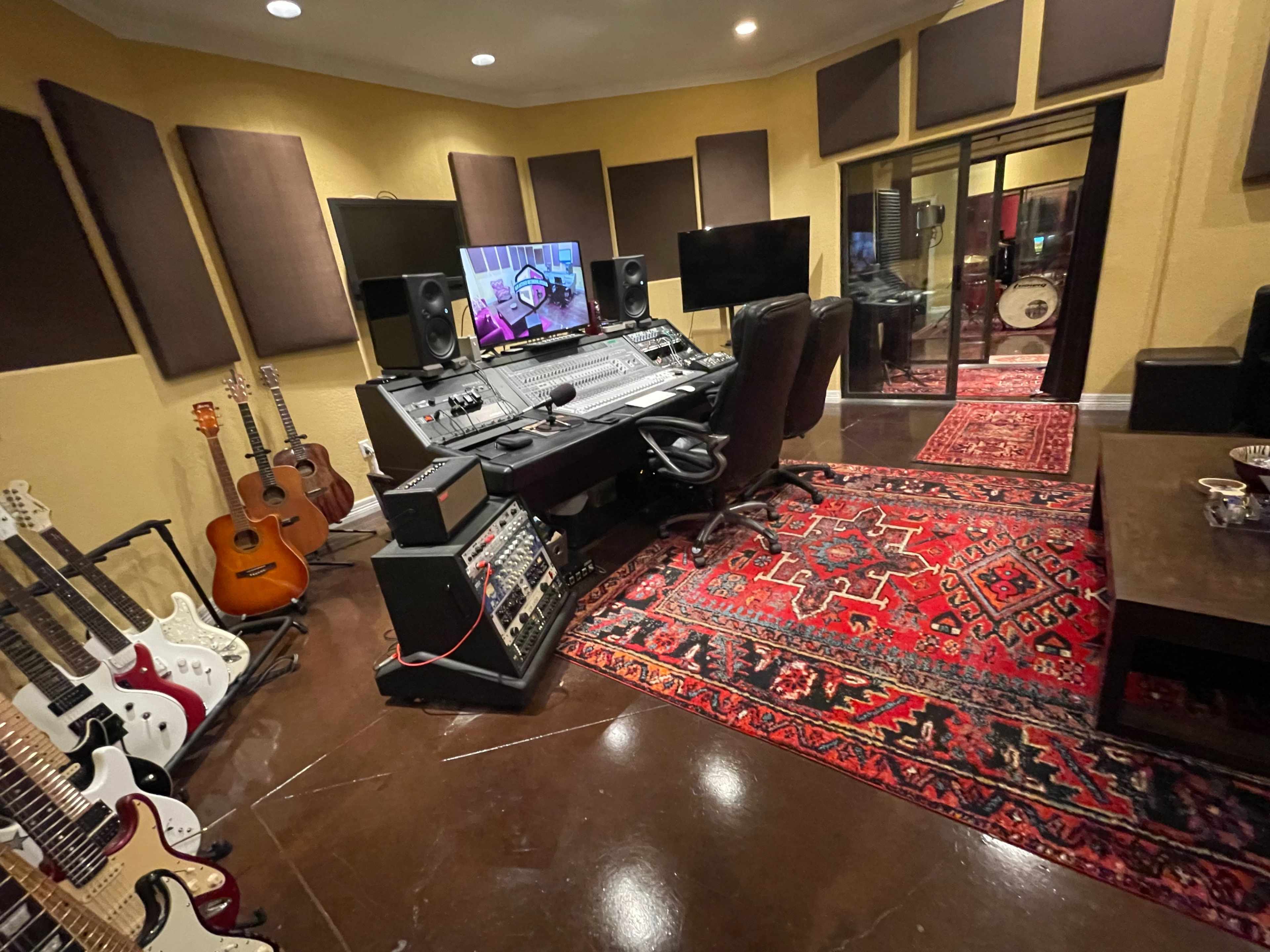 A music recording studio with a mixing console, multiple guitars, soundproofing panels, and a large area rug.