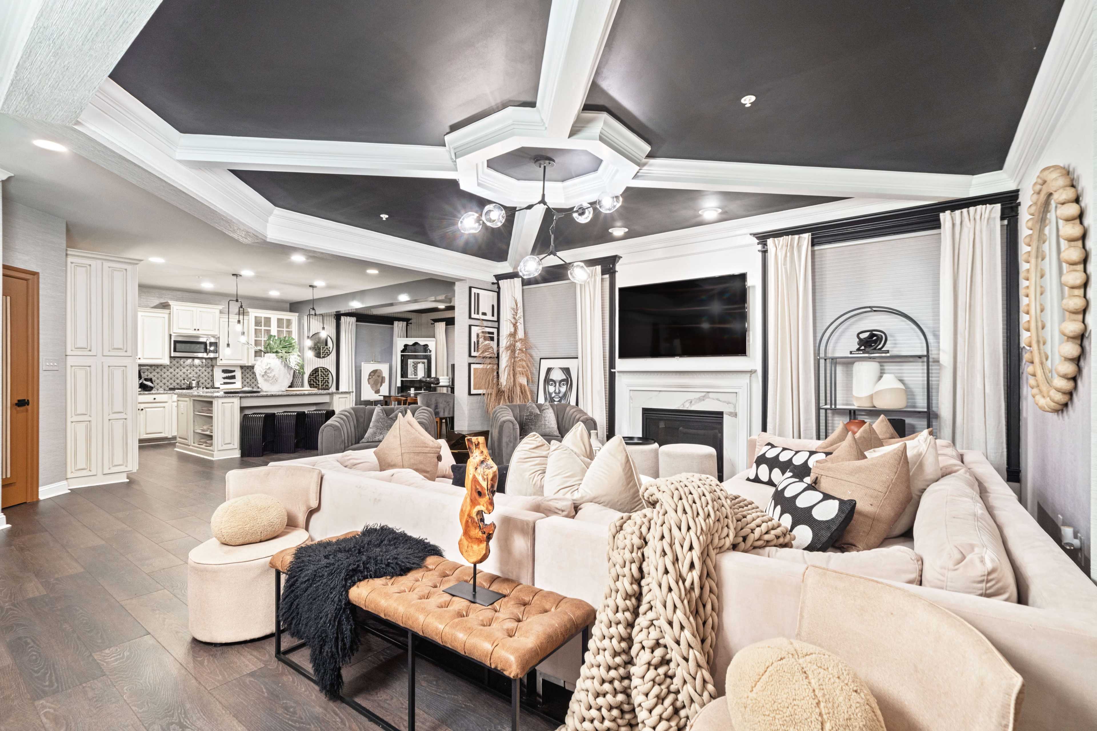 A modern living room features a large sectional sofa, a coffee table with decorative items, and a kitchen area visible in the background.