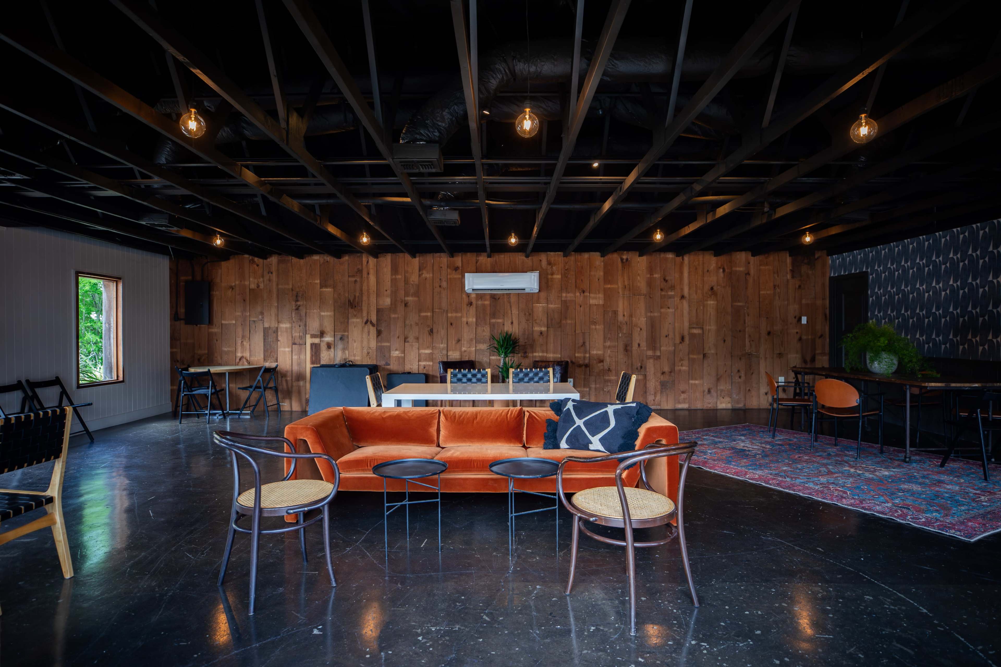 The image shows a spacious interior lounge area featuring an orange sofa, wooden accent walls, and various seating arrangements with modern decor.