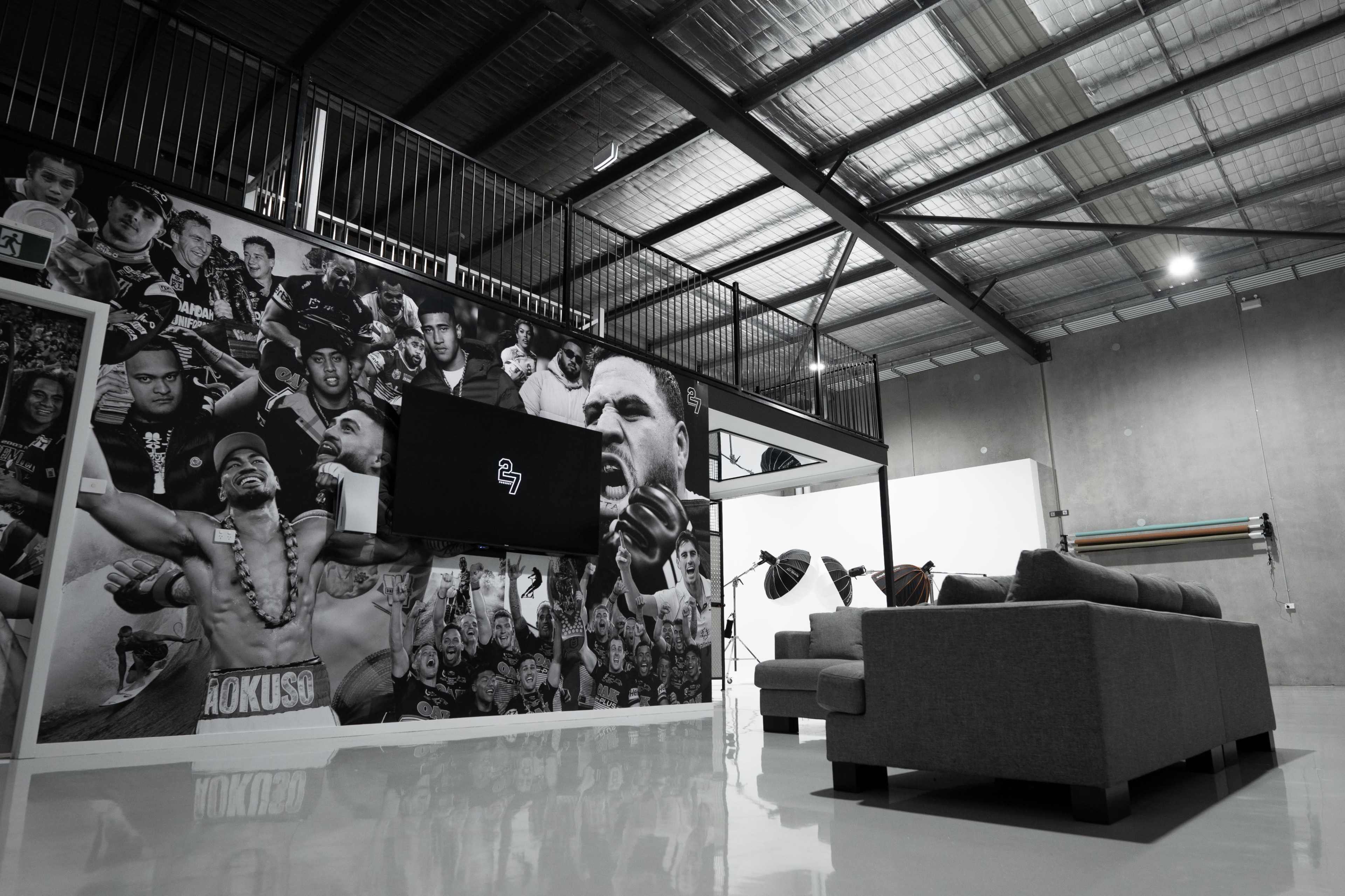 The image shows a modern indoor space featuring a large wall mural with various portraits, a mounted flat-screen TV, and a gray sofa.