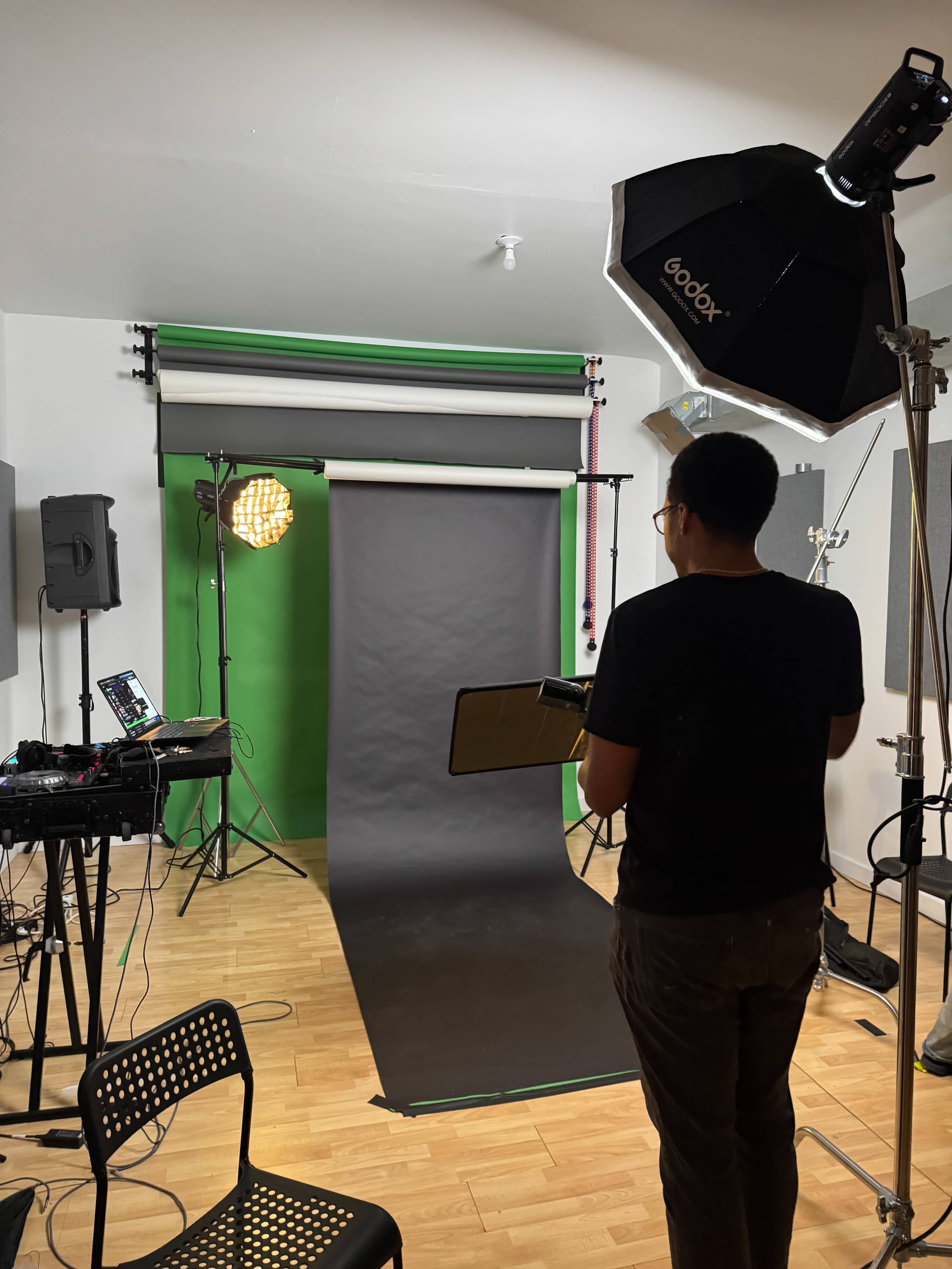 A person stands in a photography studio, preparing a black backdrop while various lights and equipment are set up around them.