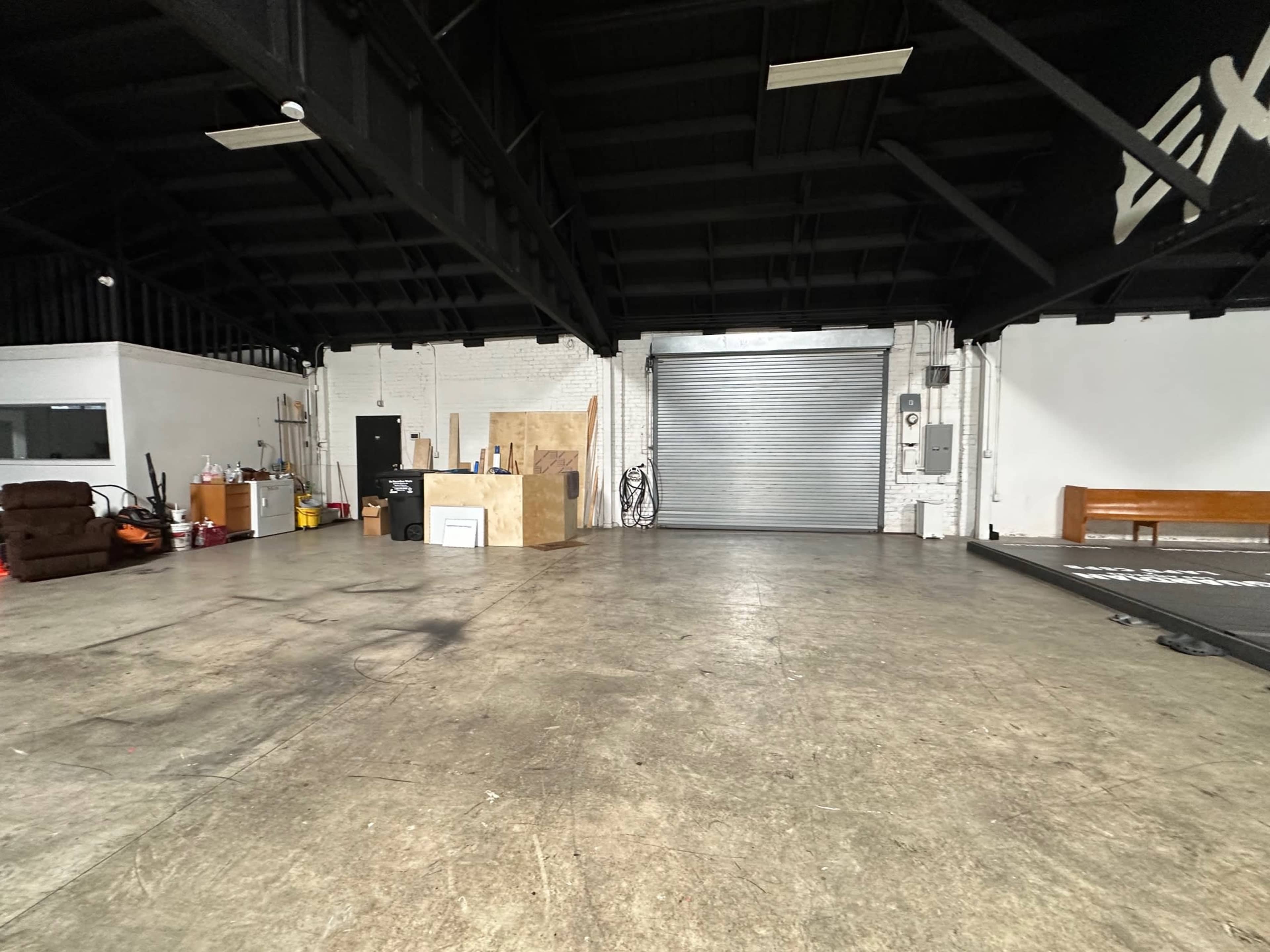 The image shows a spacious industrial interior with polished concrete flooring, a large open area, and a rolling garage door in the background.