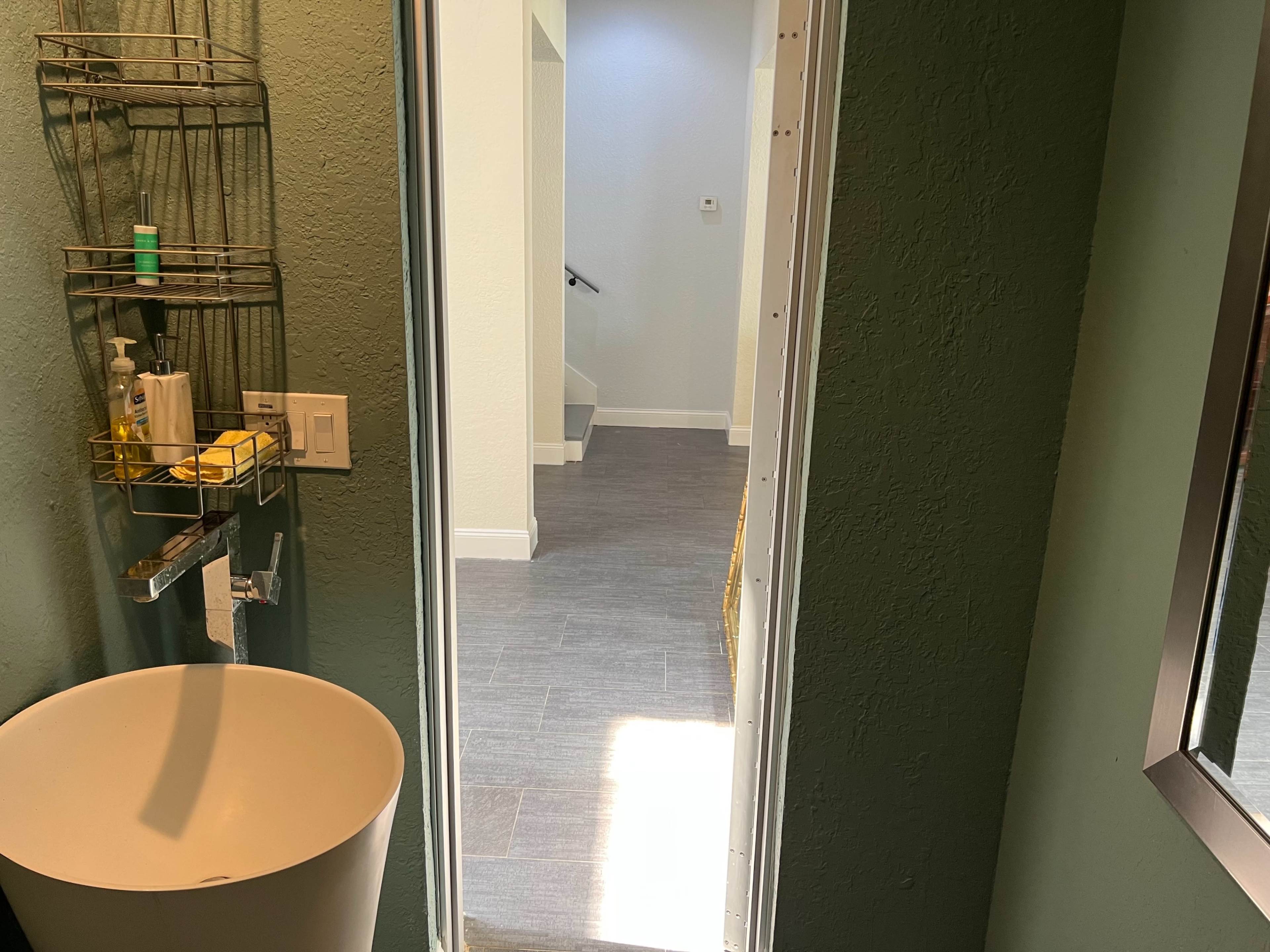 A view from a bathroom with a round sink and a hallway leading to a staircase in the background.