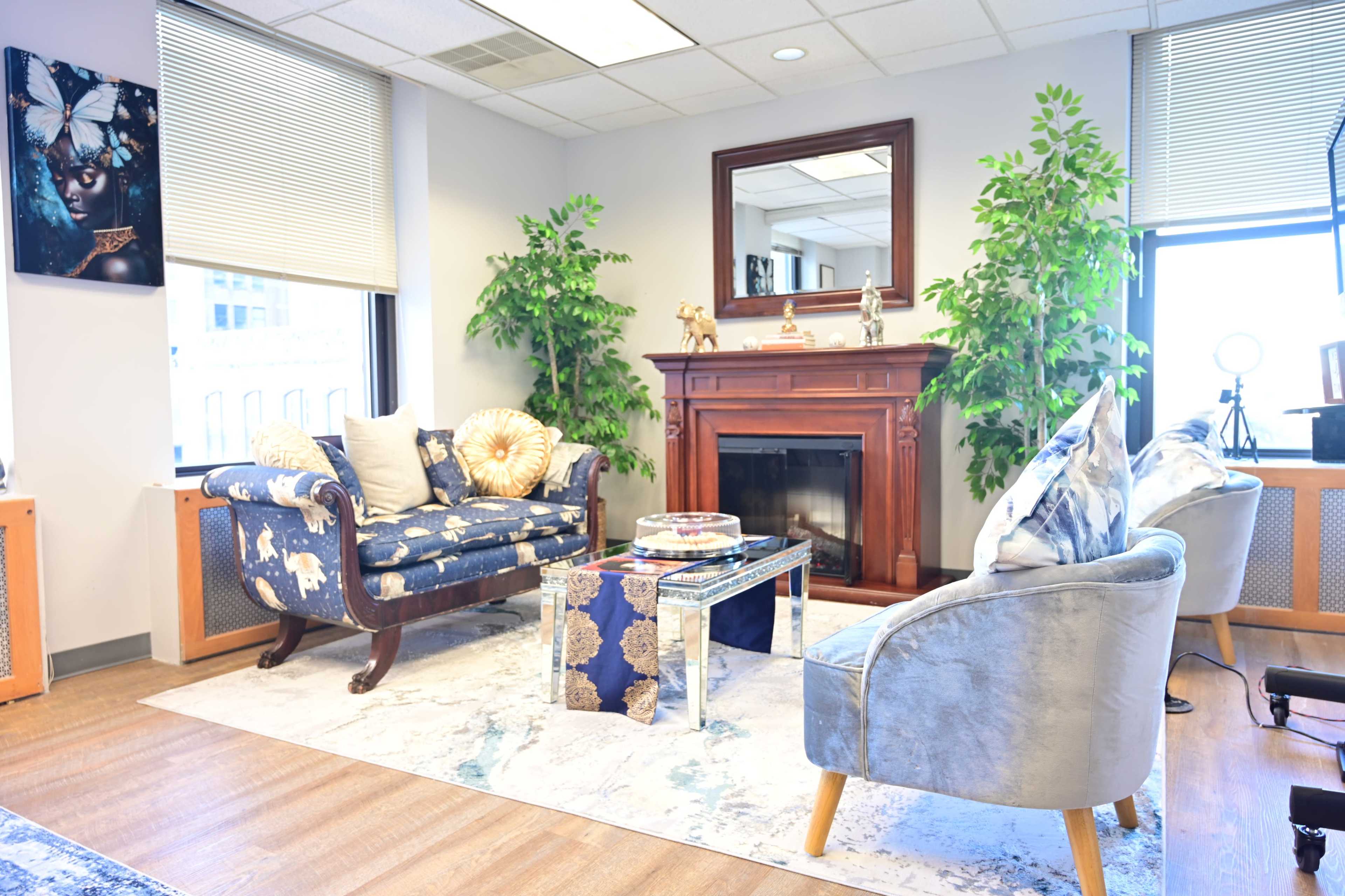 The image shows a modern, stylish living room featuring two sofas, a decorative rug, a fireplace, and indoor plants.