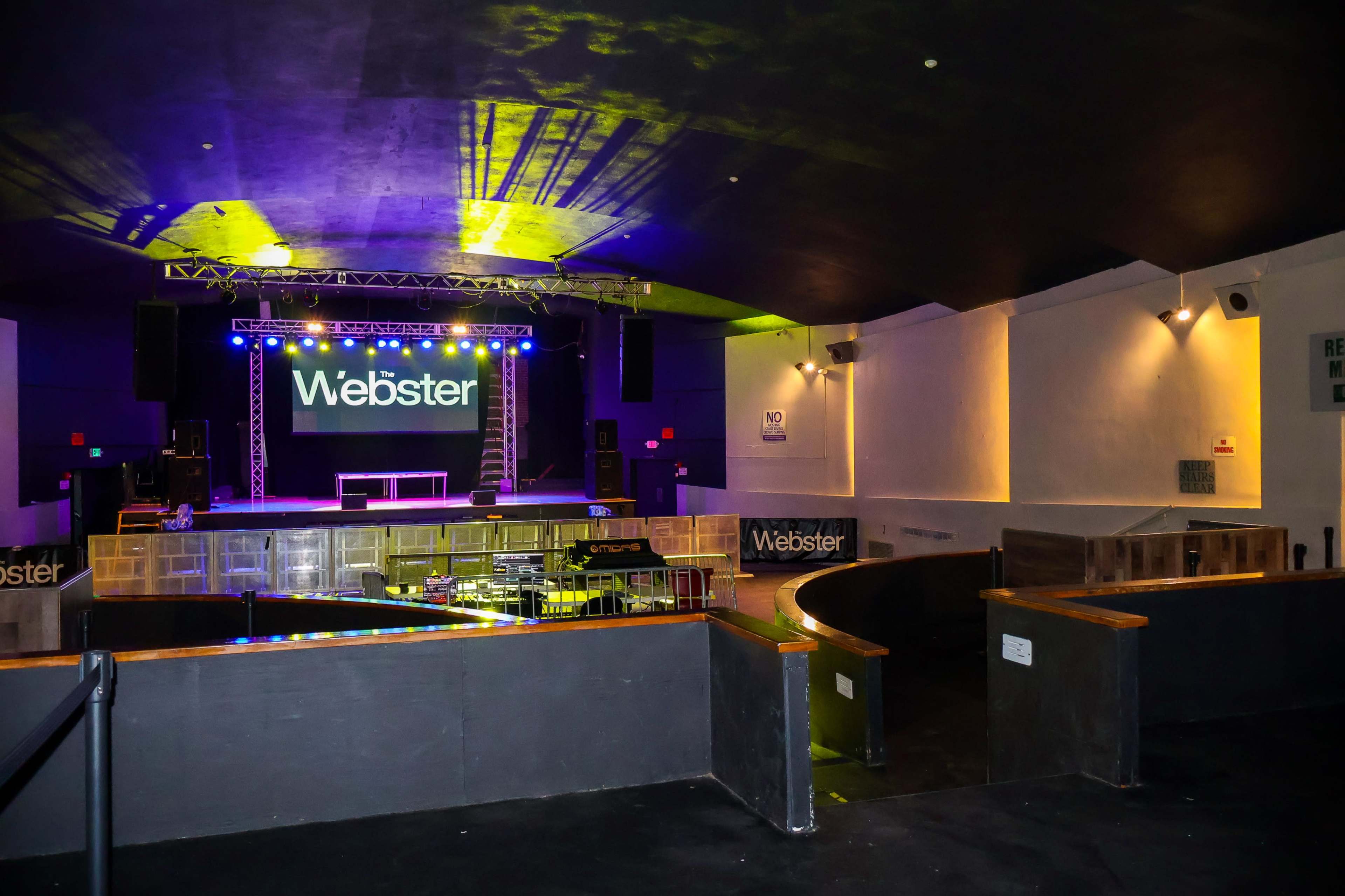 An interior view of a concert venue featuring a stage with the name "Webster" lit up in bright colors and empty seating areas.