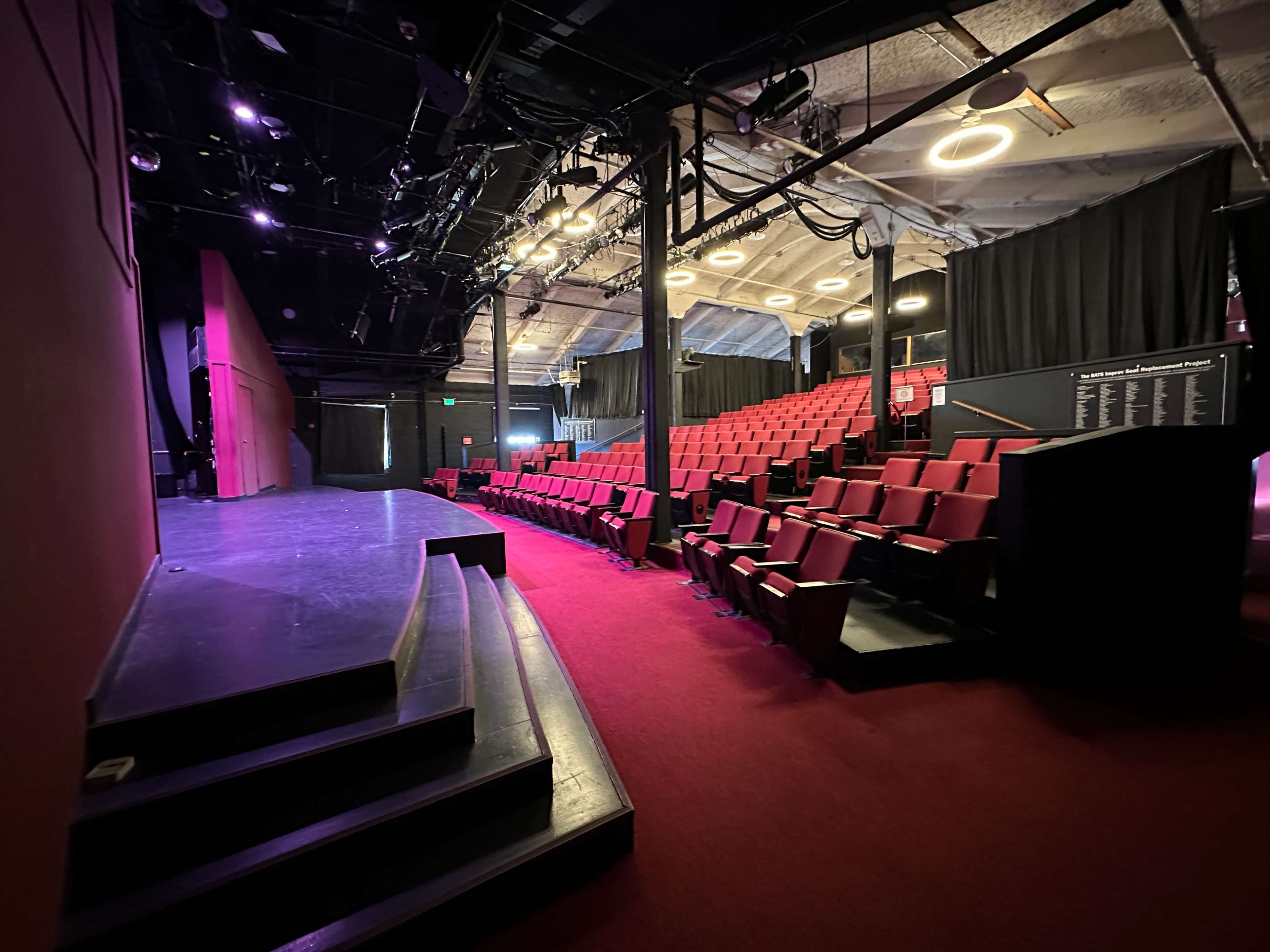 The interior of a theater with a stage, red seating, and dimly lit surroundings.