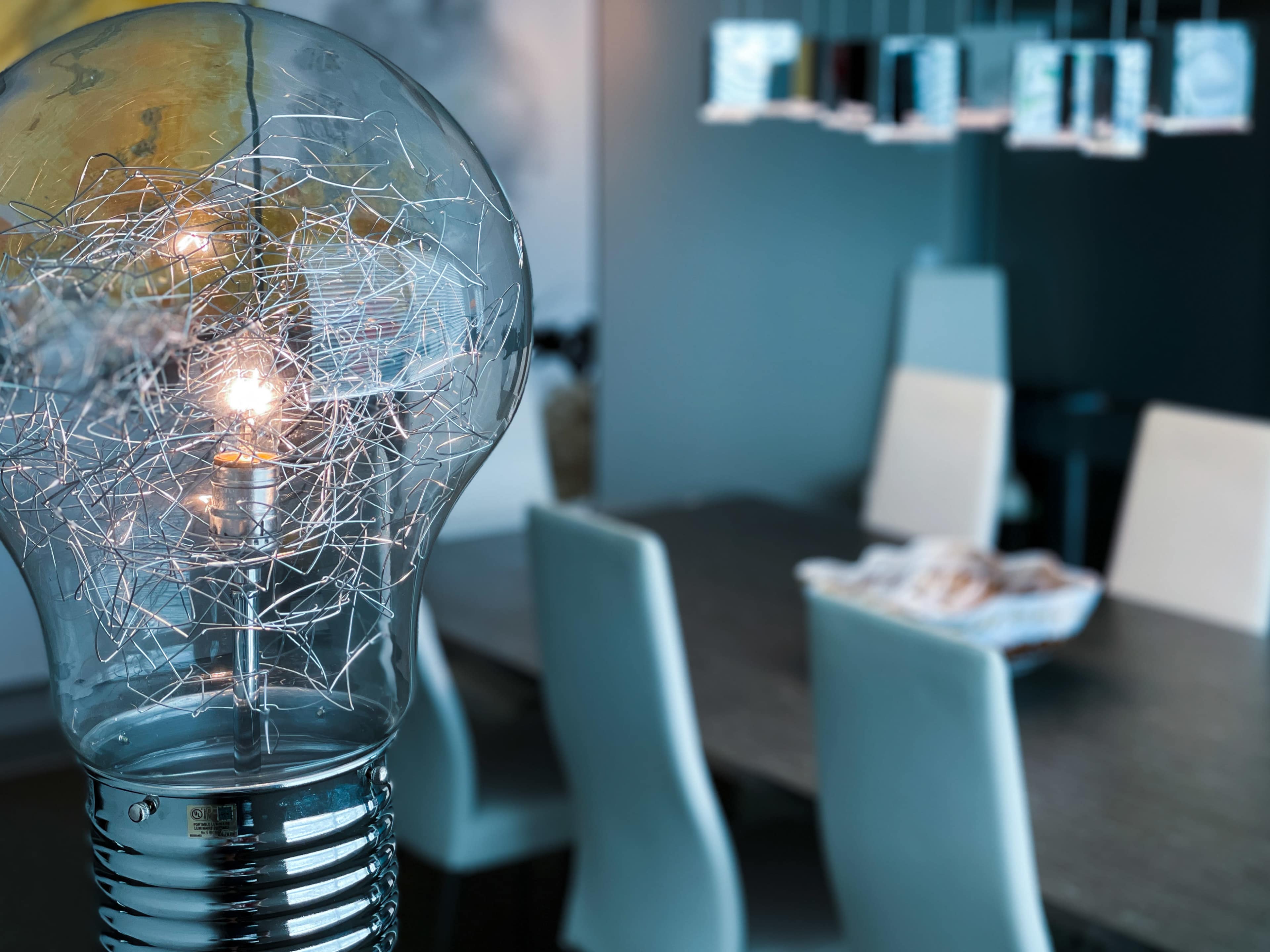 A decorative light bulb with visible filament illuminates a modern dining area featuring a table and white chairs.