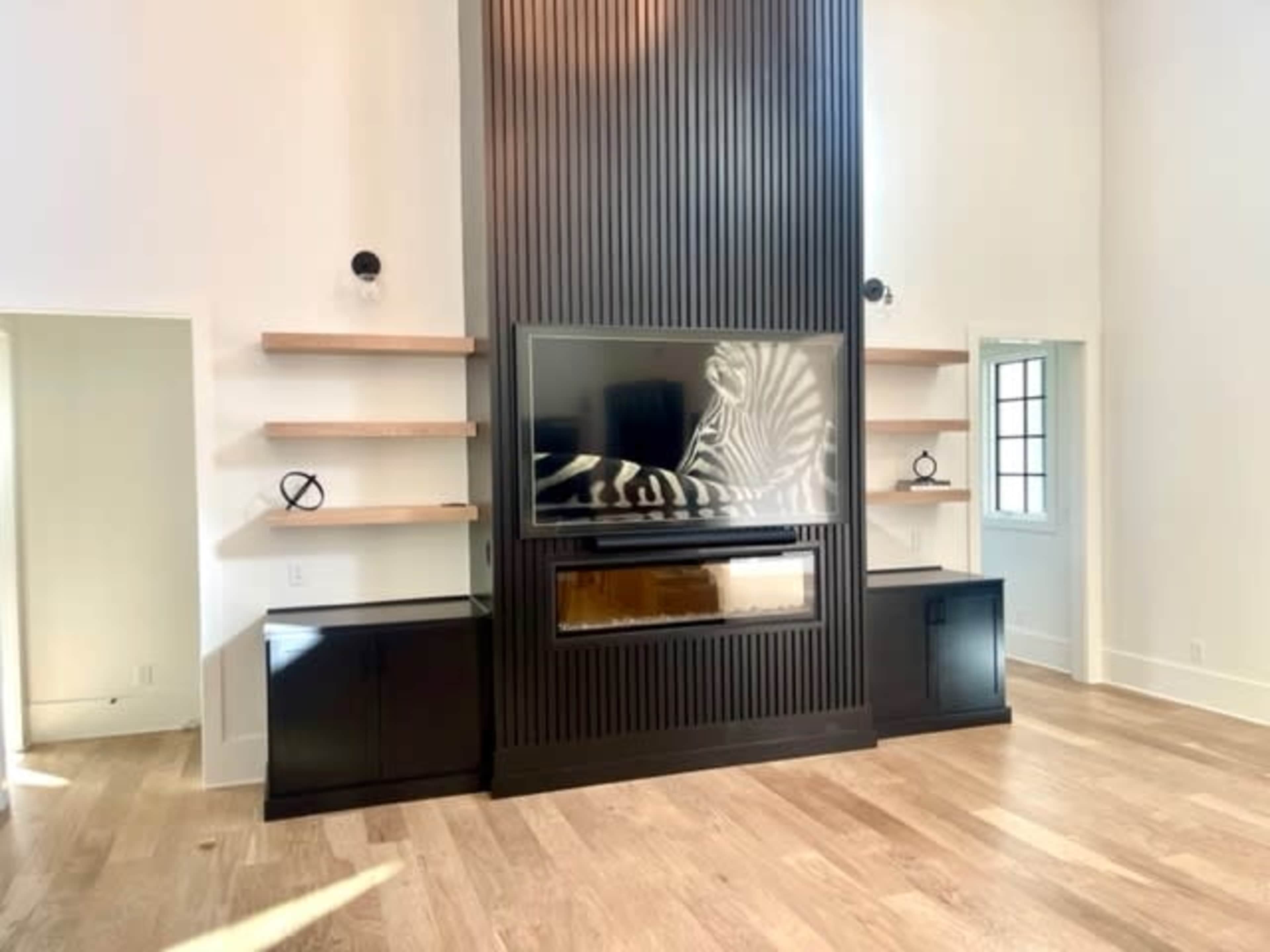 The image shows a modern living room with a vertical slatted feature wall housing a television and an electric fireplace, flanked by floating shelves and dark cabinetry.
