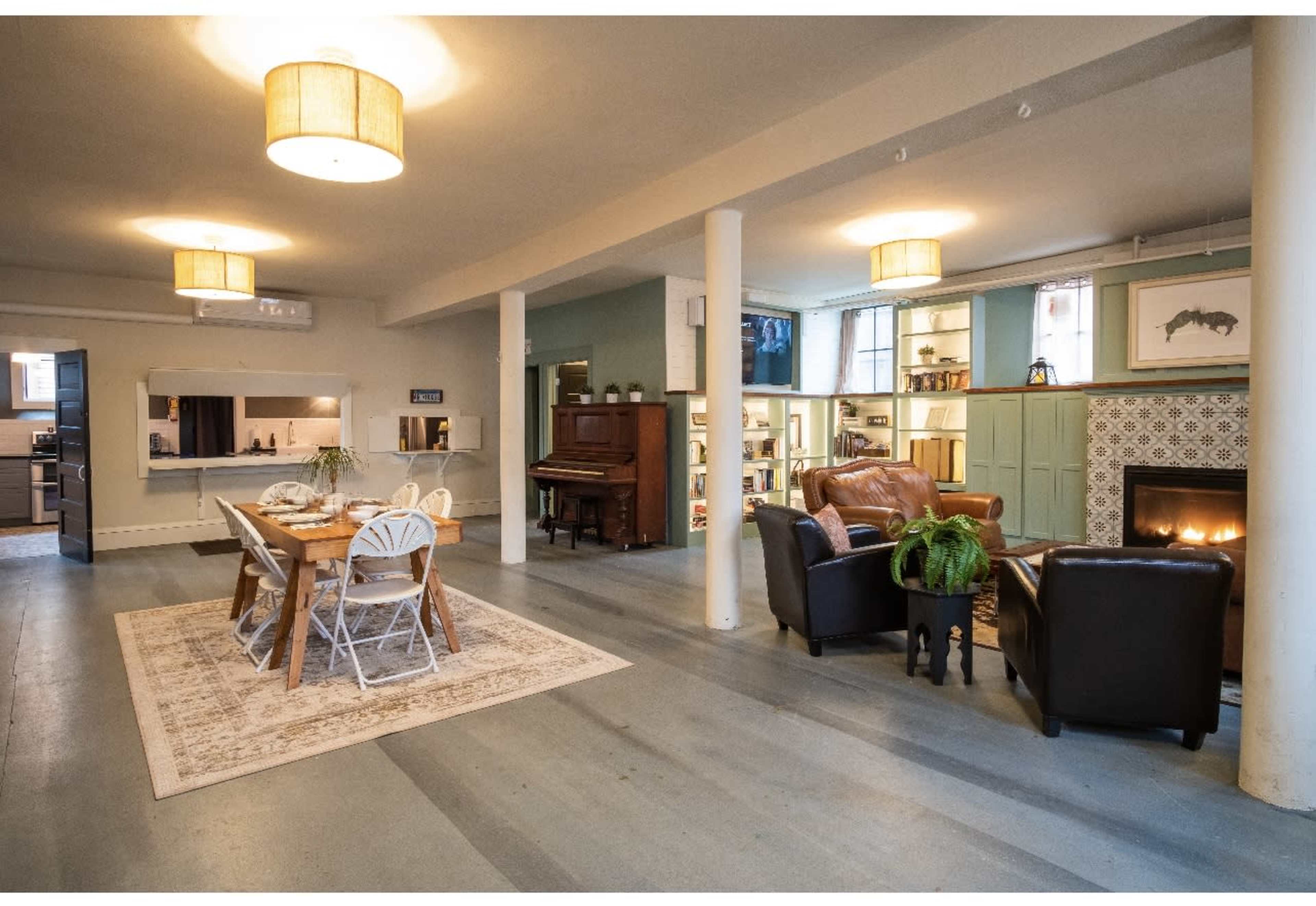A spacious, modern living area with a dining table, a piano, and a fireplace, featuring light fixtures and a cozy seating arrangement.