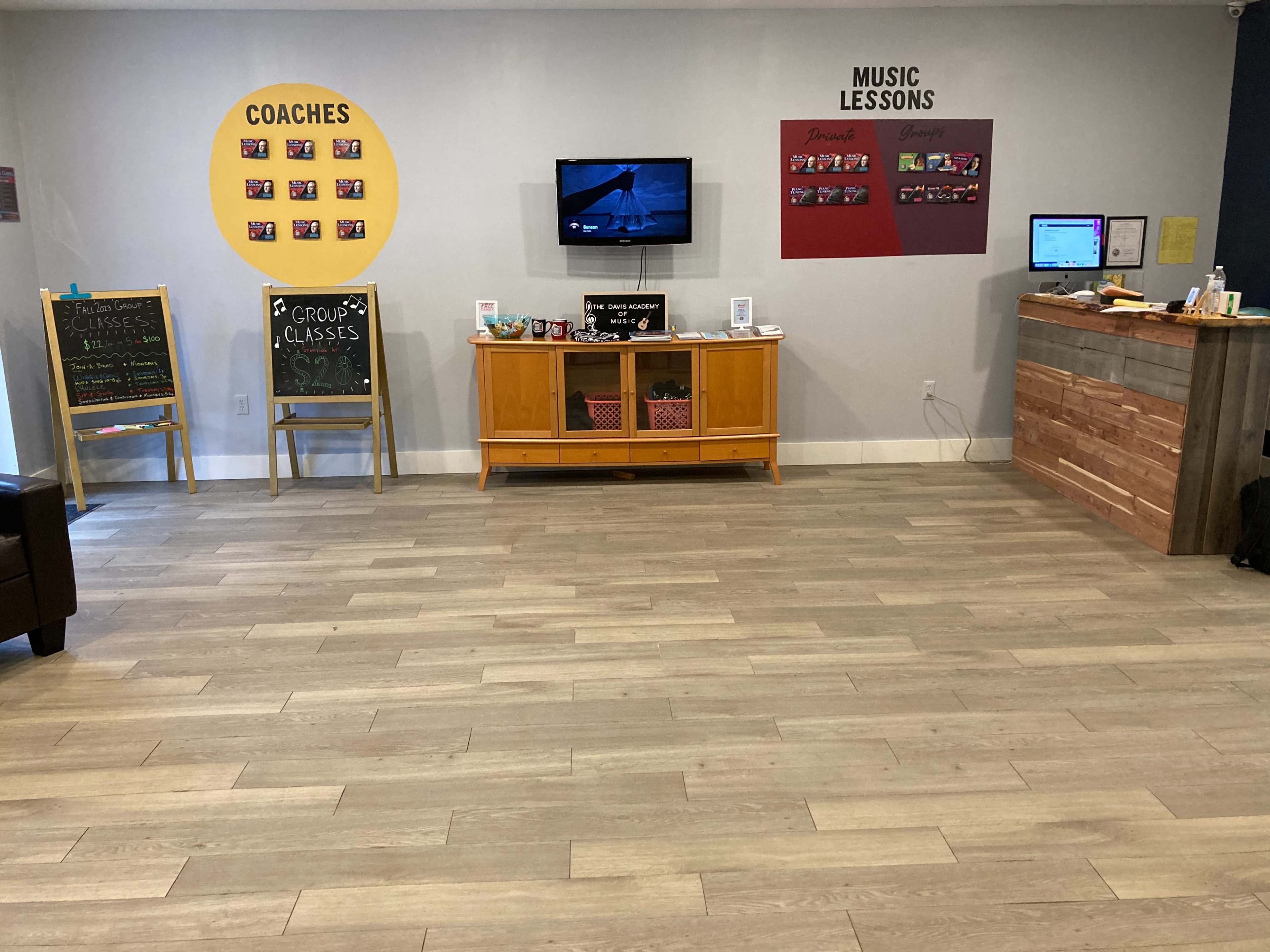 The image shows a music studio reception area featuring a variety of signage, a television, a wooden counter, and a wooden cabinet with storage.