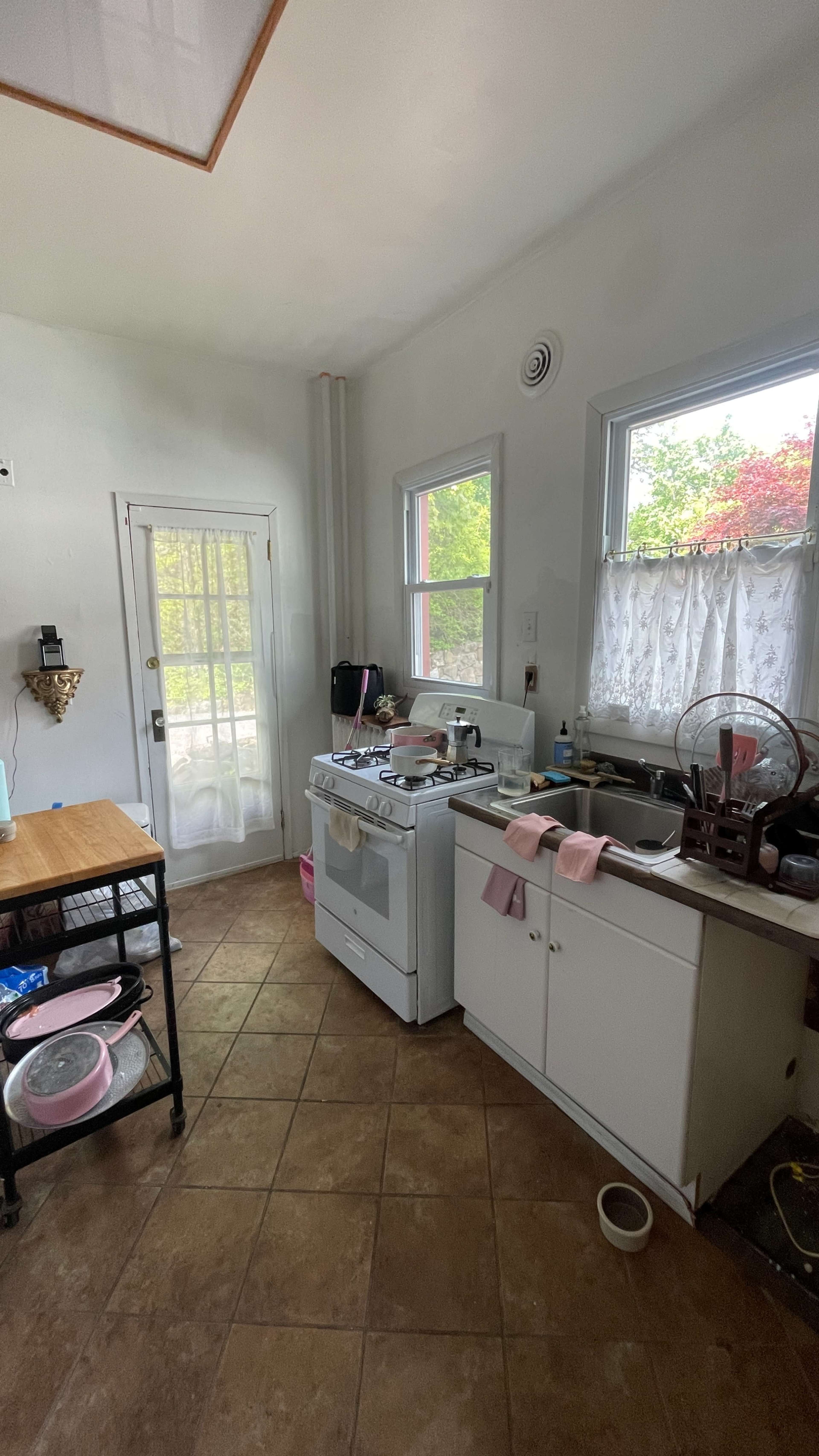 The image shows a kitchen with a stove, a sink, and a small table, along with dishes and kitchen utensils on the counters.