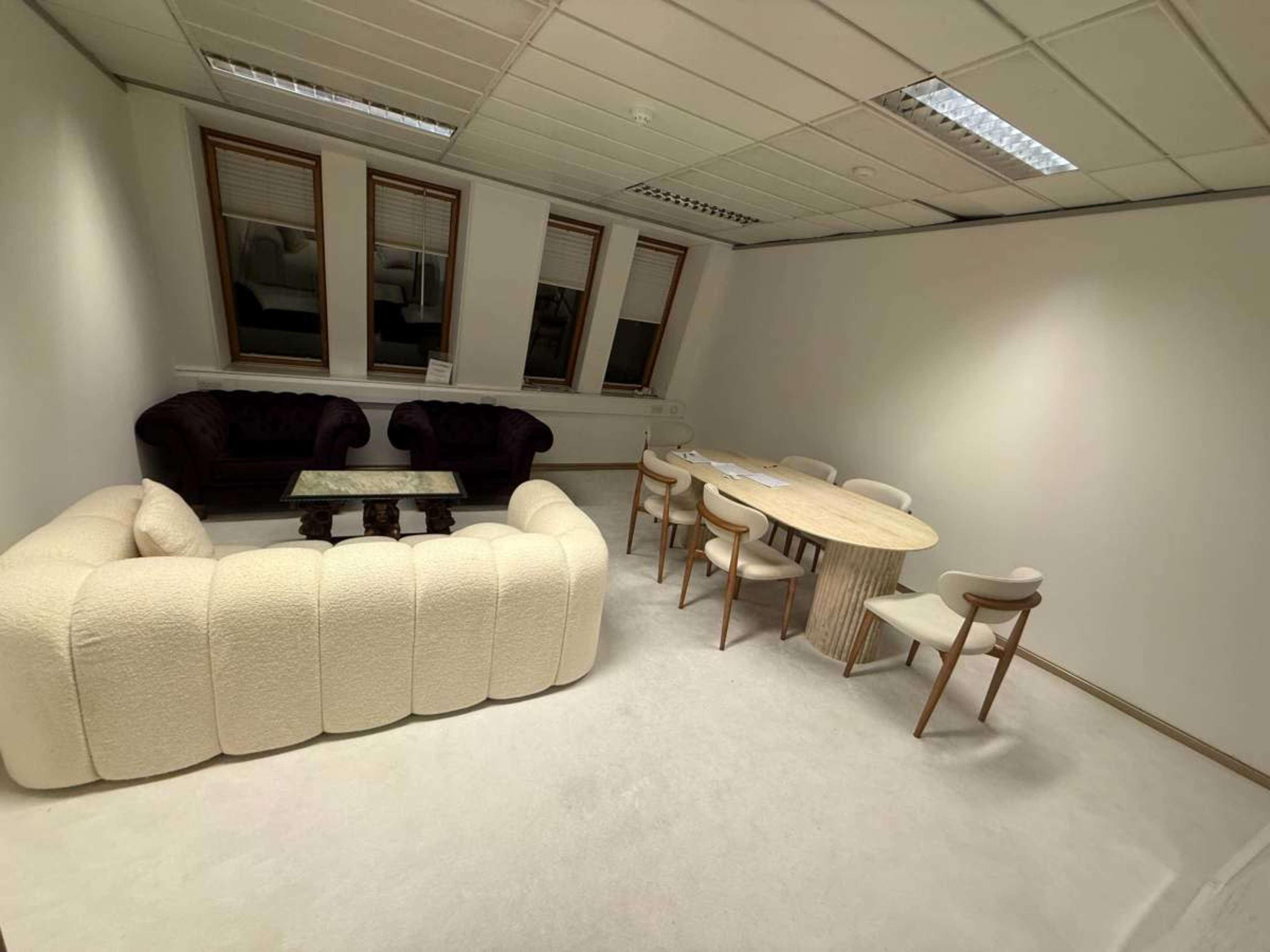 The image shows a minimalist office space with a curved couch, a small glass coffee table, and a round dining table surrounded by chairs.