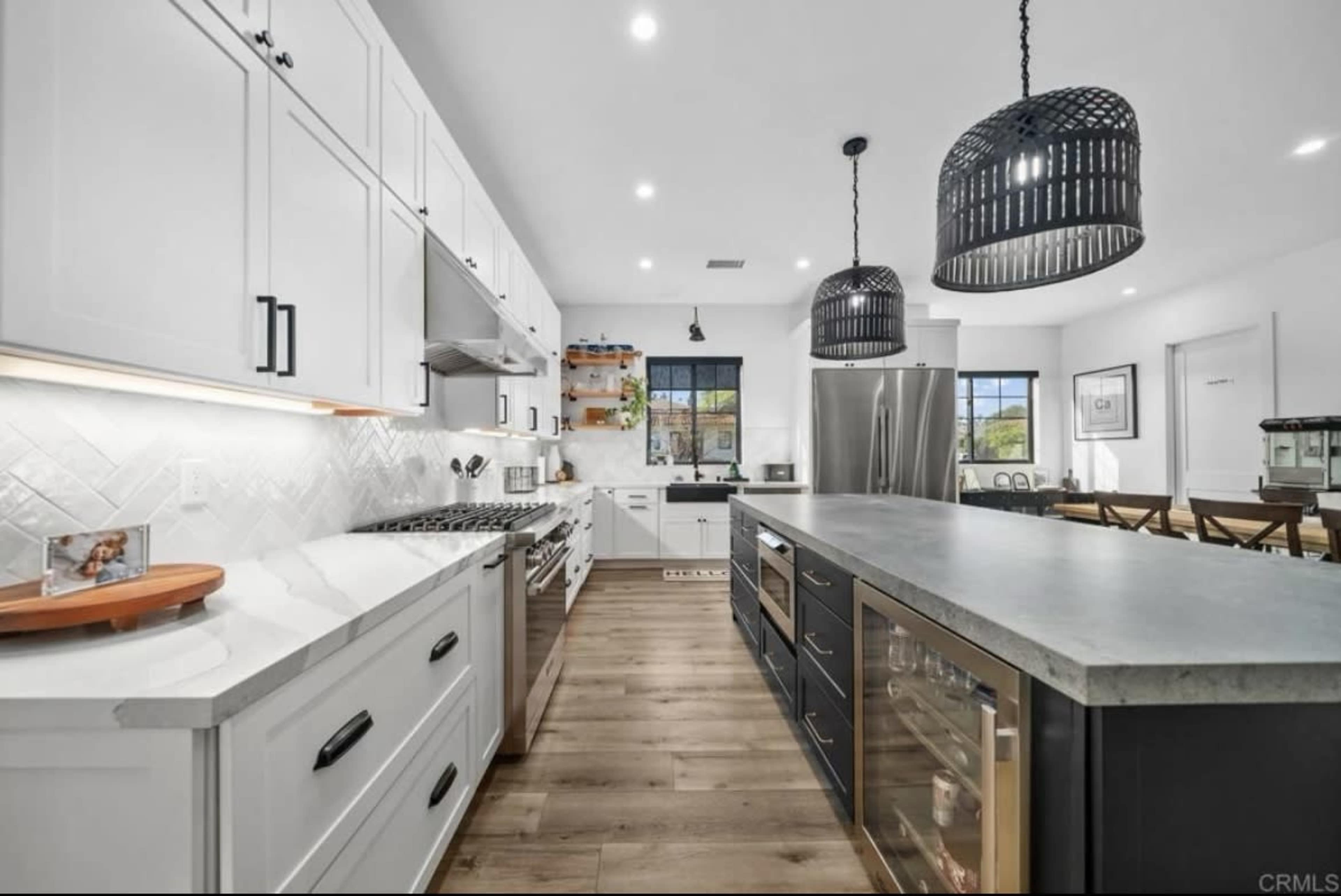 The image shows a modern kitchen featuring white cabinets, a large central island with a concrete countertop, and two pendant lights hanging above.