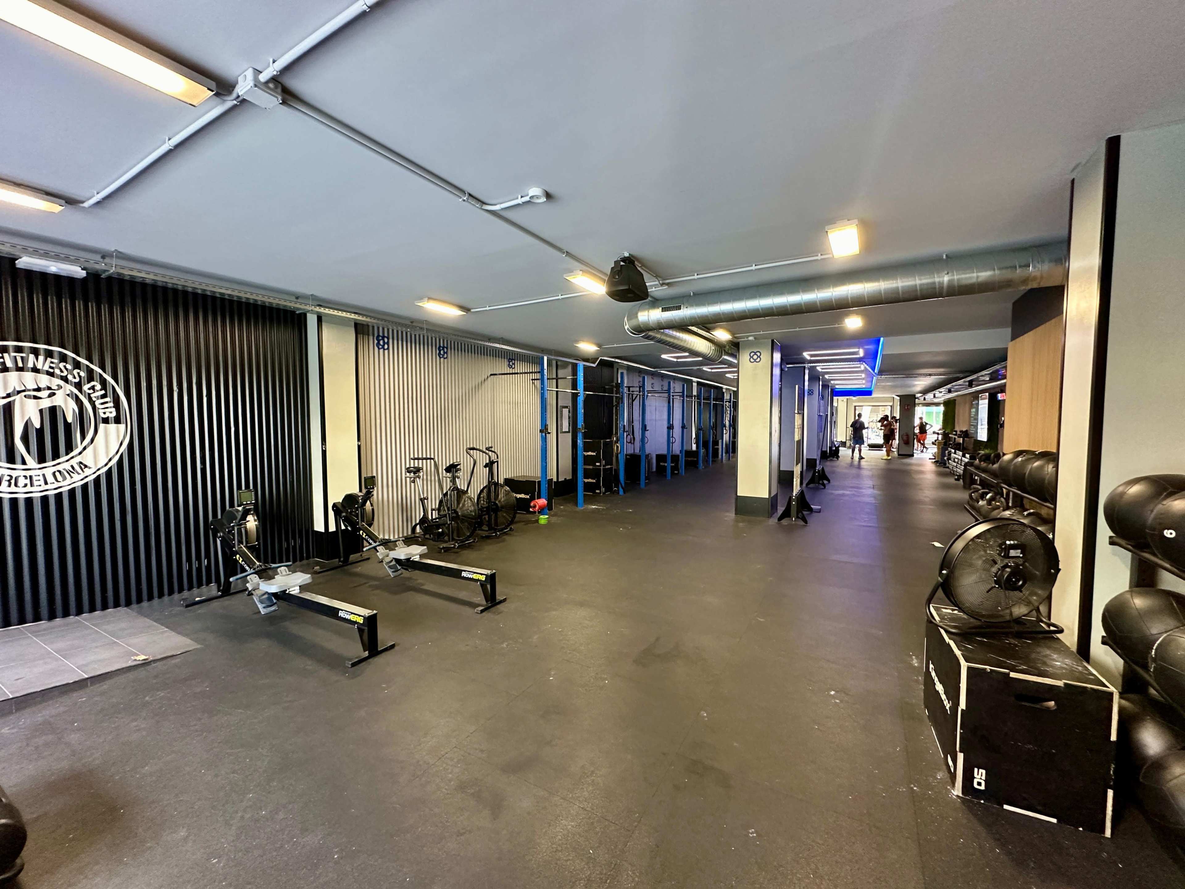 A spacious gym area with various workout equipment, including rowing machines and exercise bikes, along one side and training stations along the opposite wall.