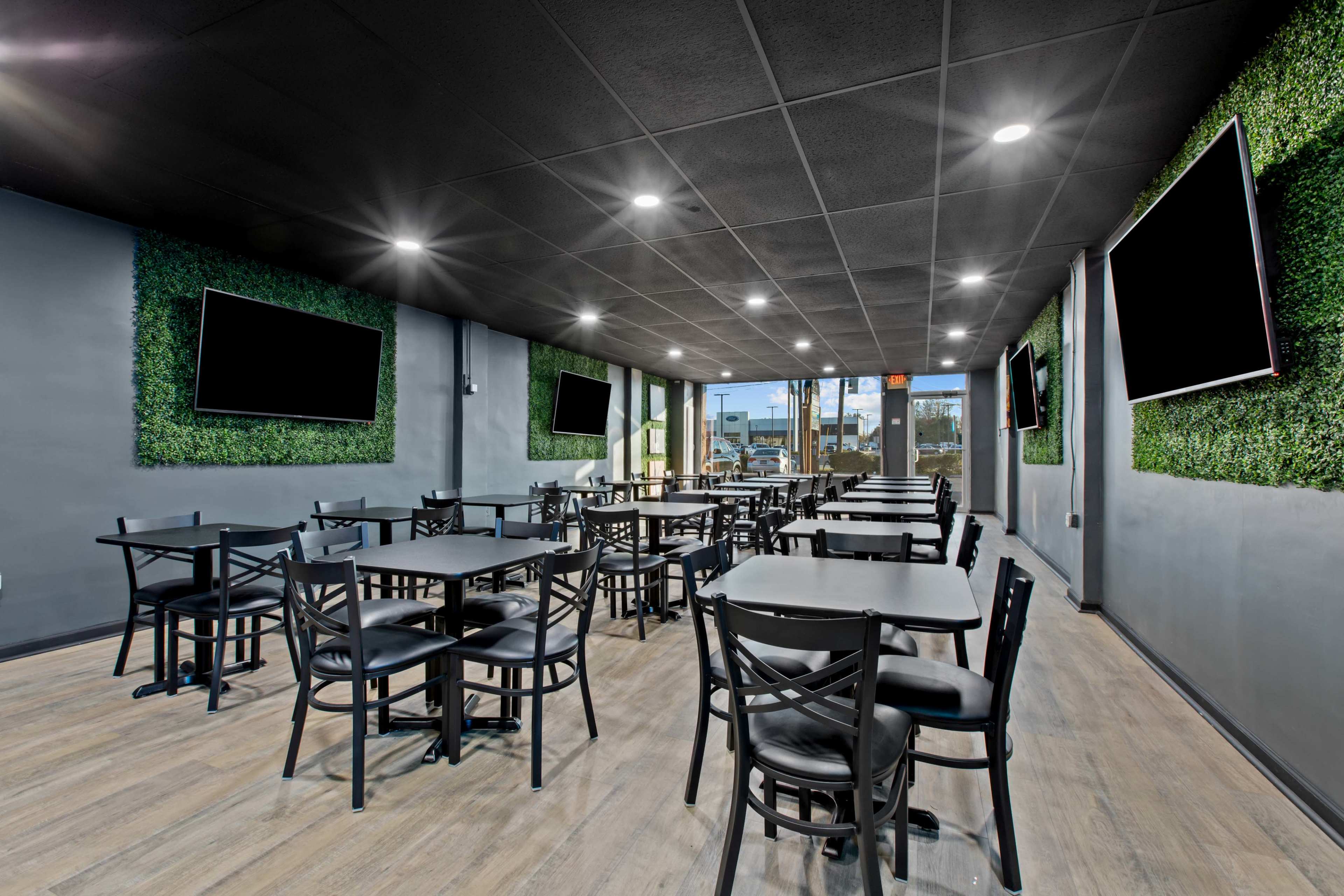 A modern dining area with black tables and chairs, featuring green wall décor and multiple flat-screen televisions.