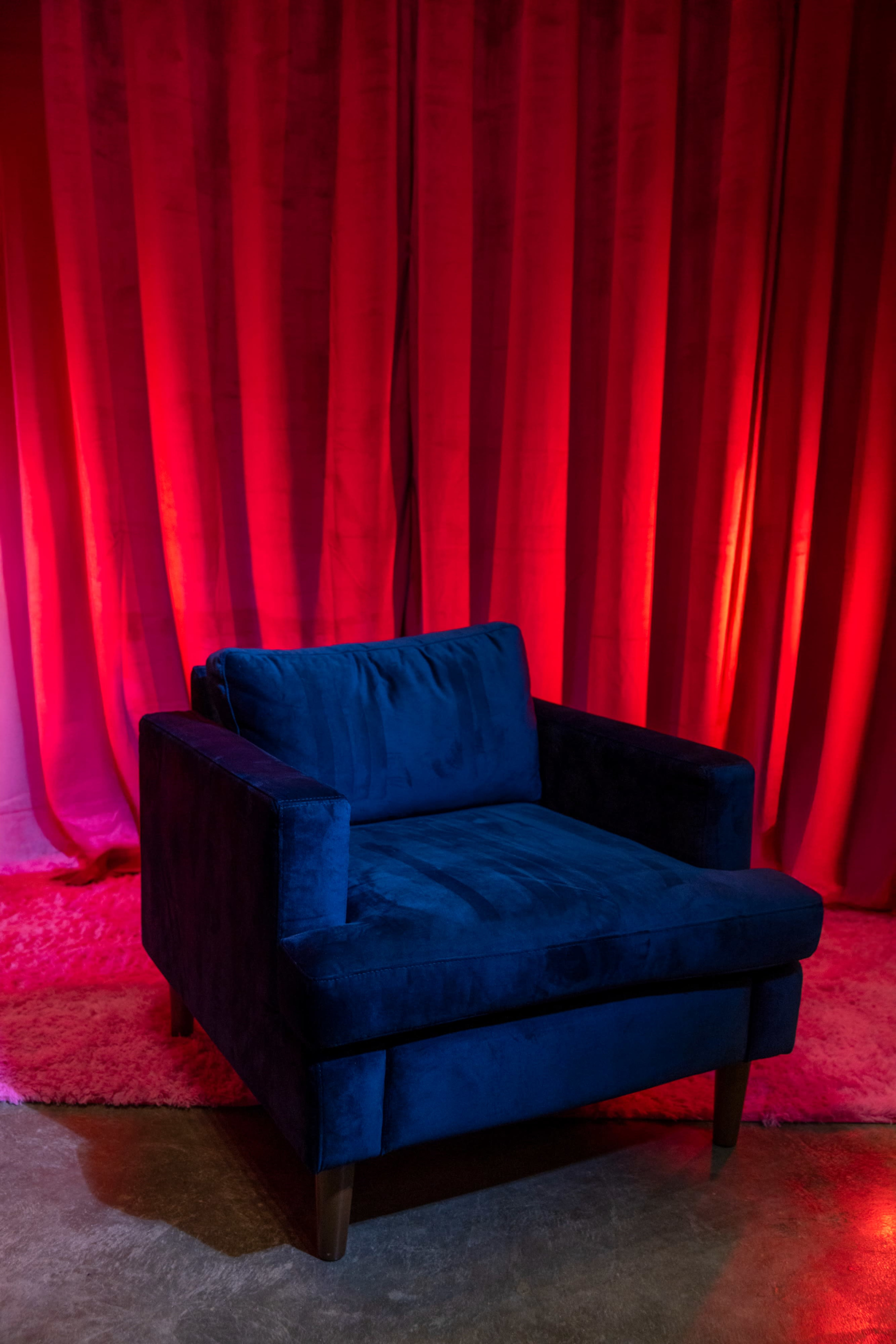 A blue upholstered armchair sits against a textured red backdrop.
