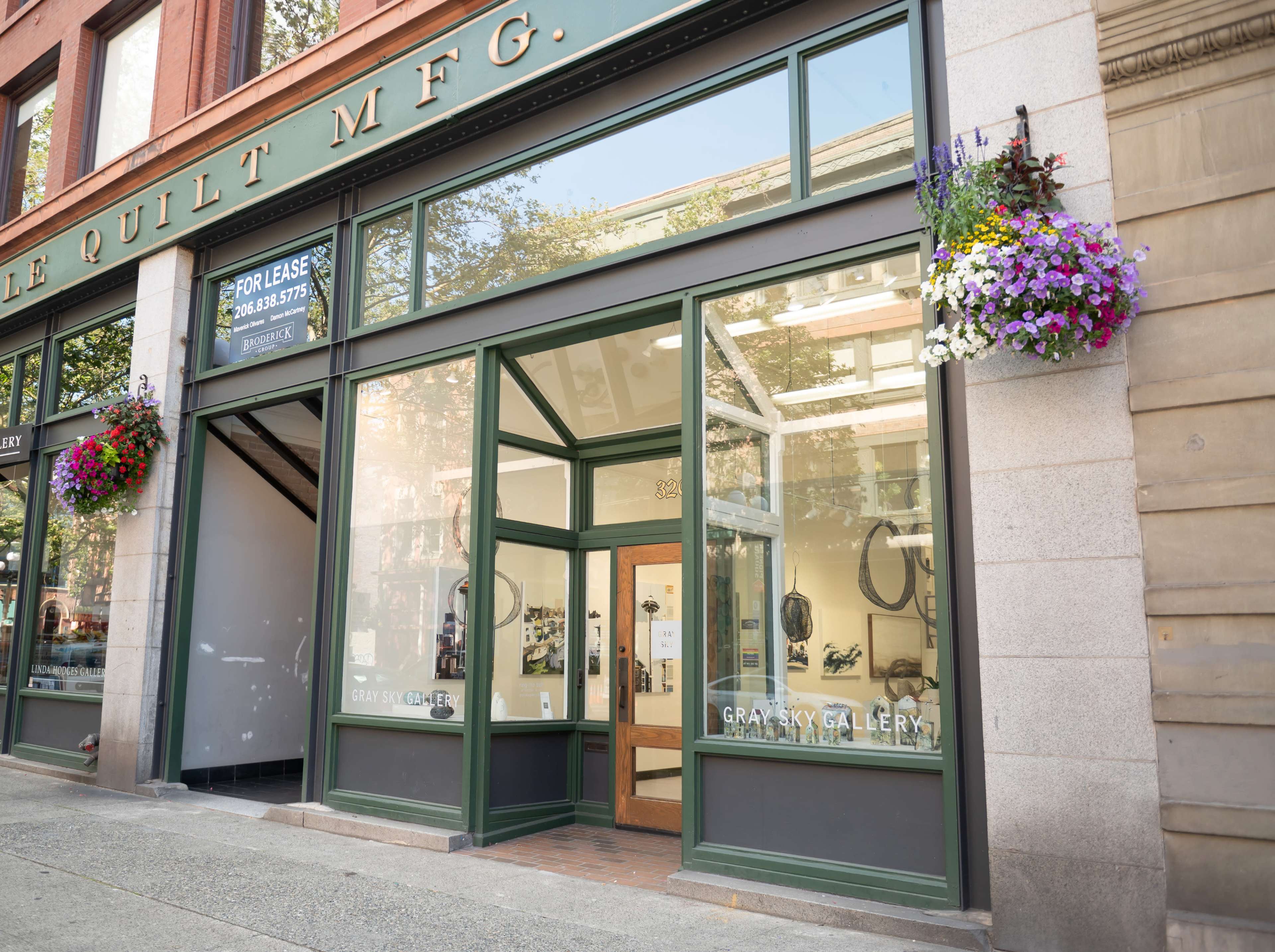 The exterior of a gallery called "Gravity Gallery," featuring large windows and flower baskets above the entrance on a city street.