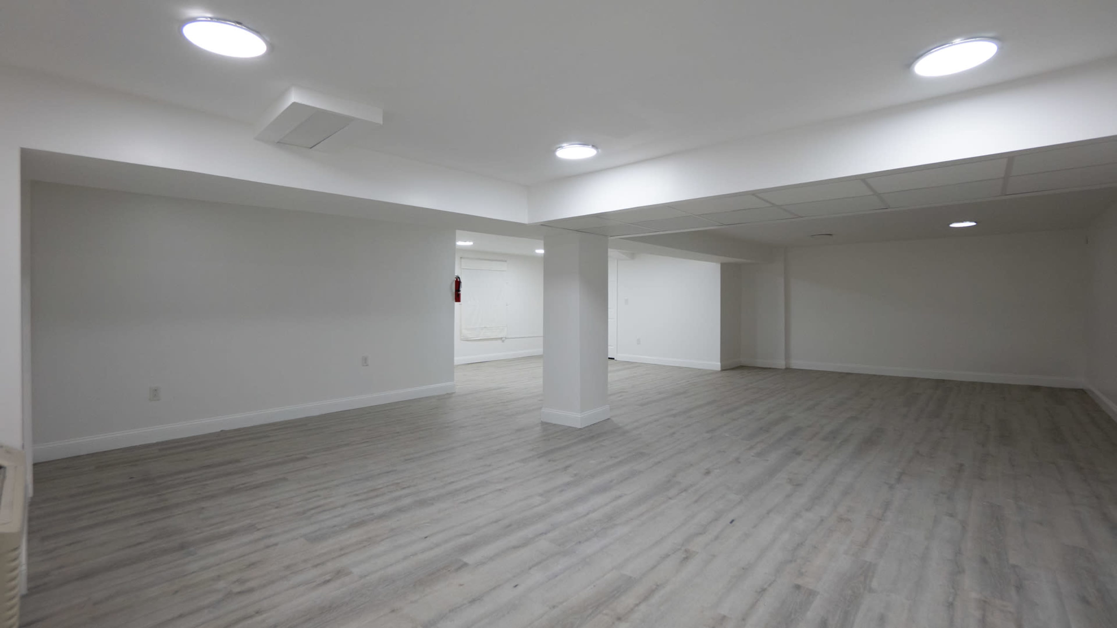 A large, empty room with light-colored wood flooring and recessed lighting on a white ceiling.