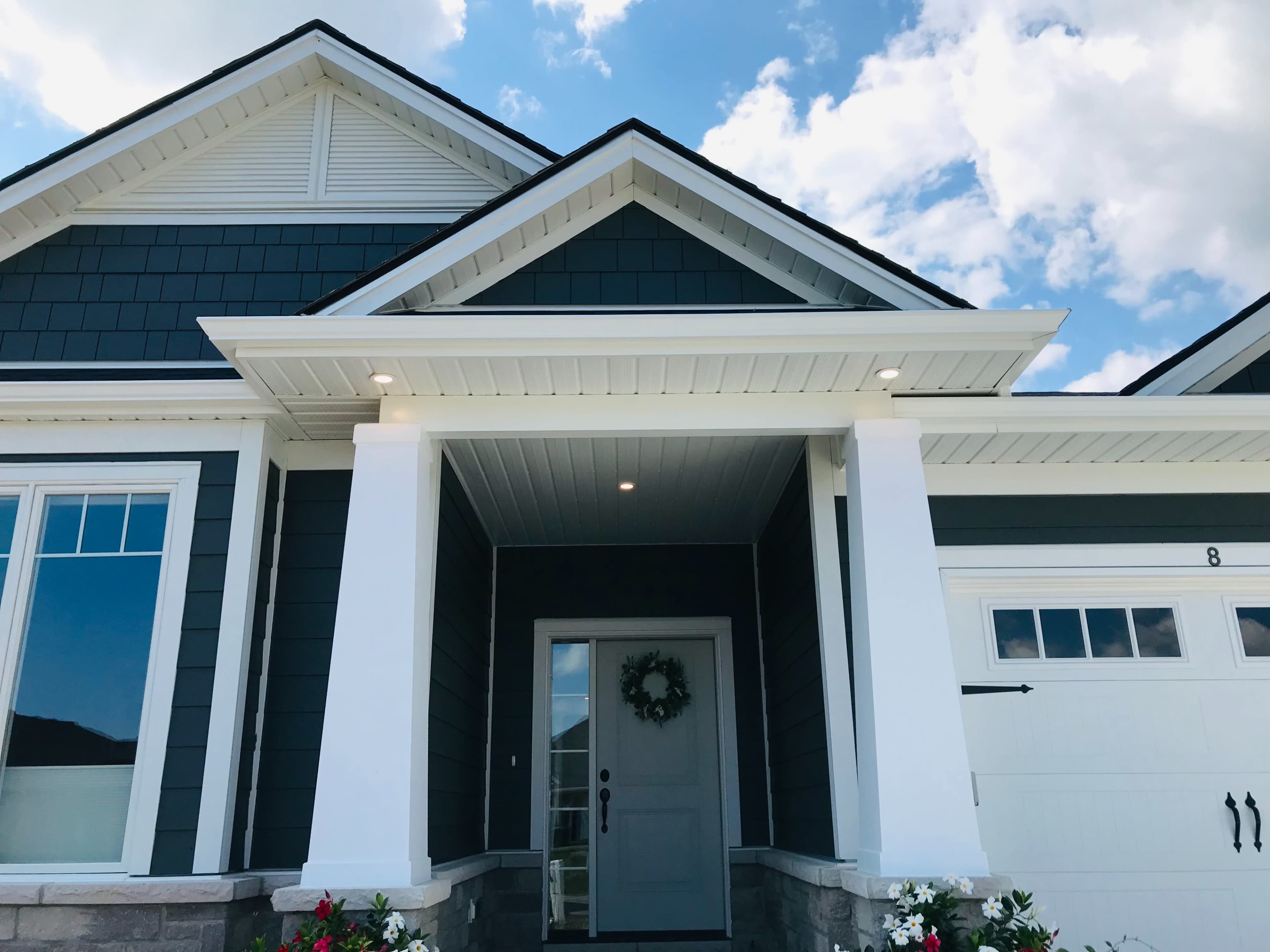 A modern house entrance with a gray exterior, white columns, and a decorative wreath on the front door.