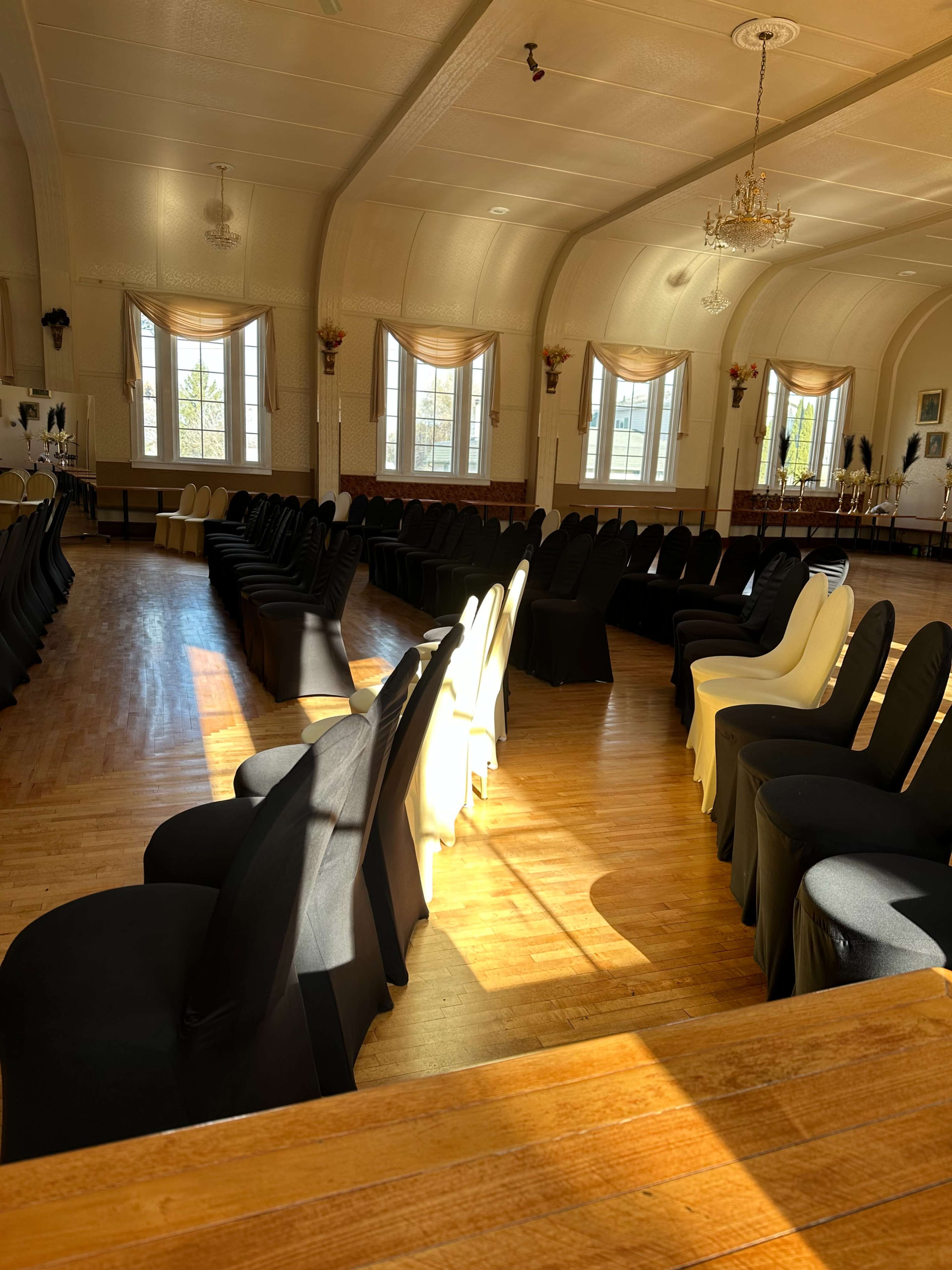 A spacious, elegant hall arranged with alternating black and white chairs set in curved rows, illuminated by natural light from large windows.