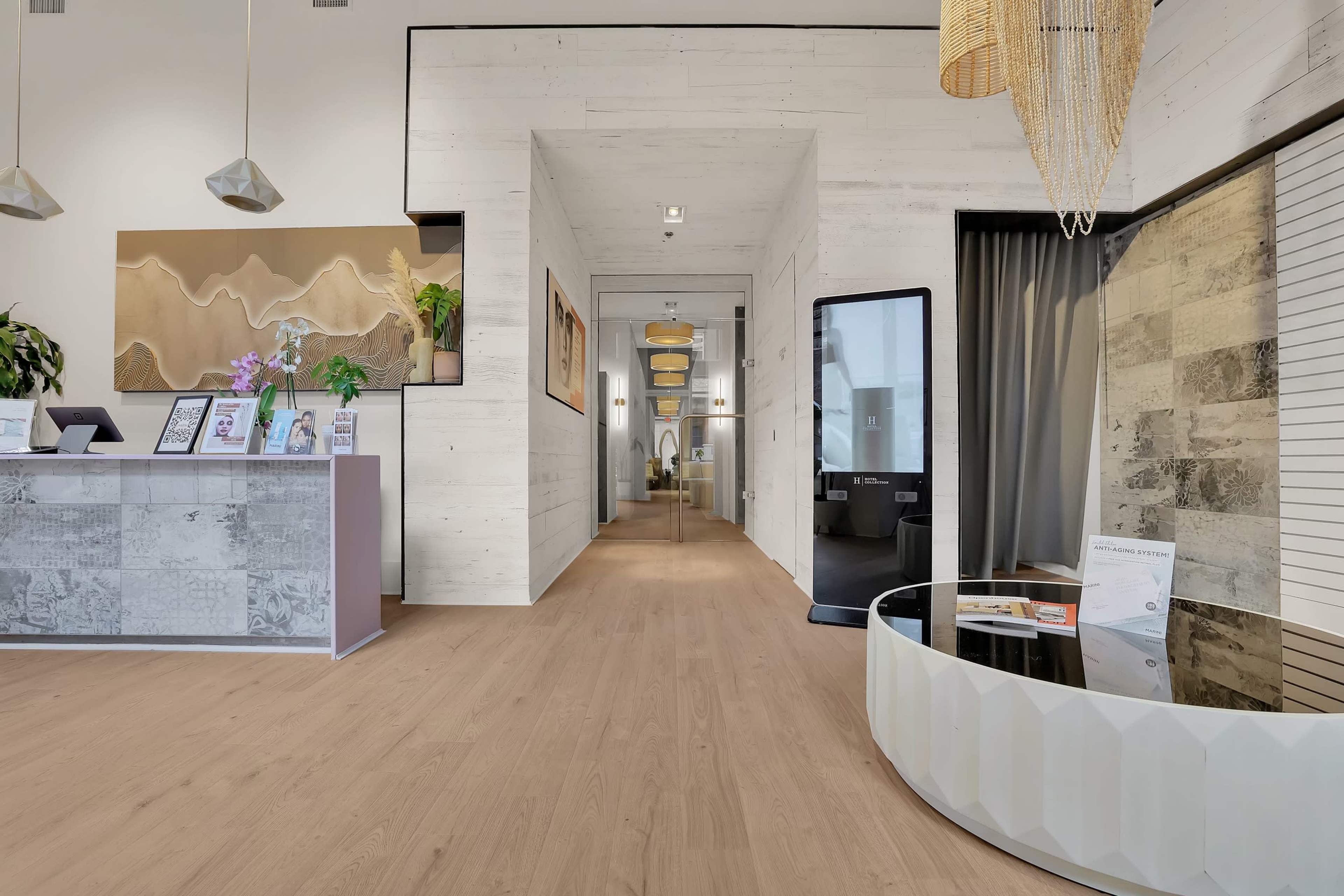 The image shows a modern interior space featuring a reception area with a sleek front desk, large decorative art pieces on the walls, and a long hallway leading to additional rooms.