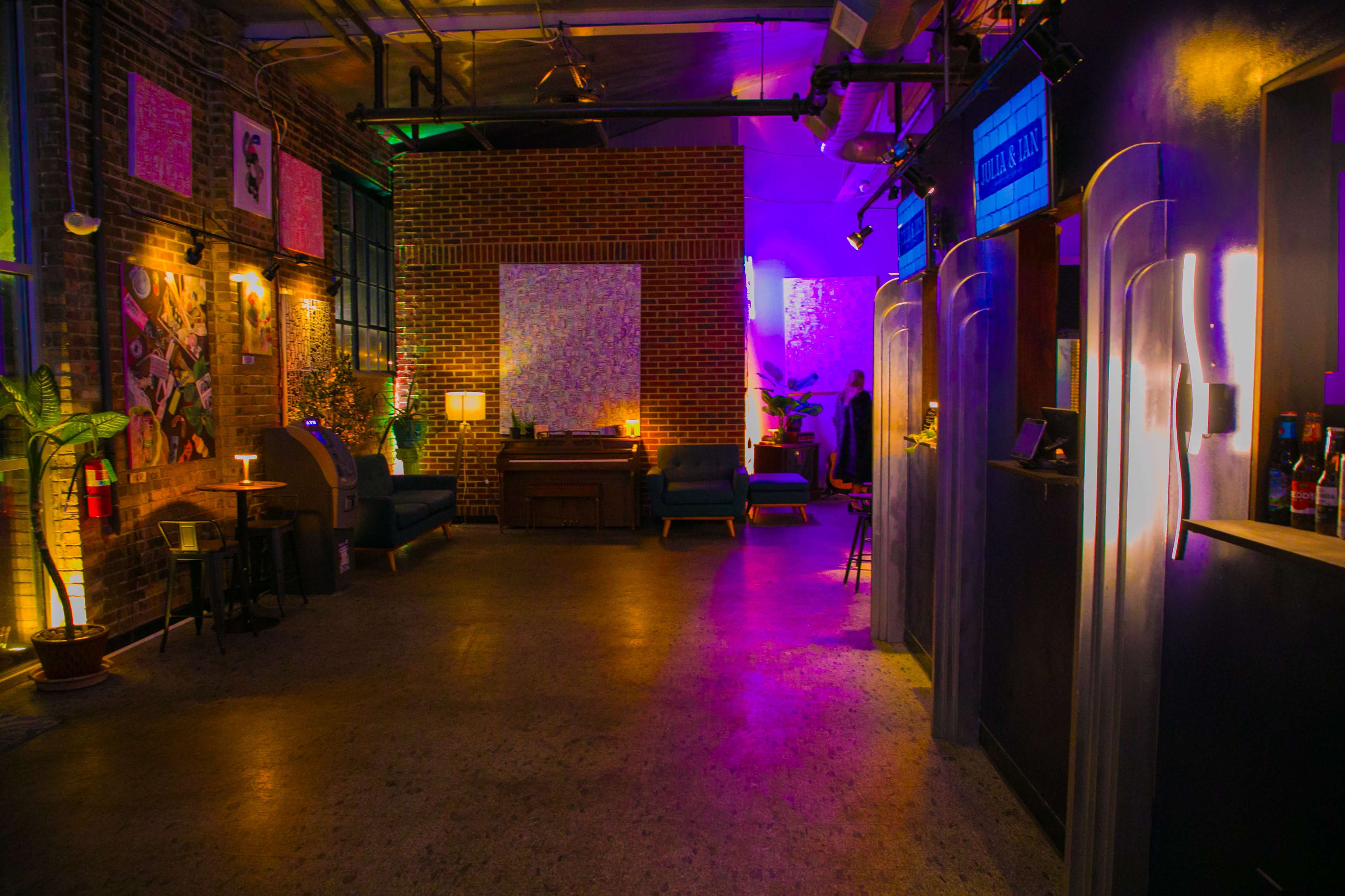 The image shows a modern interior space with exposed brick walls, colorful lighting, and various seating arrangements, creating a lively atmosphere.