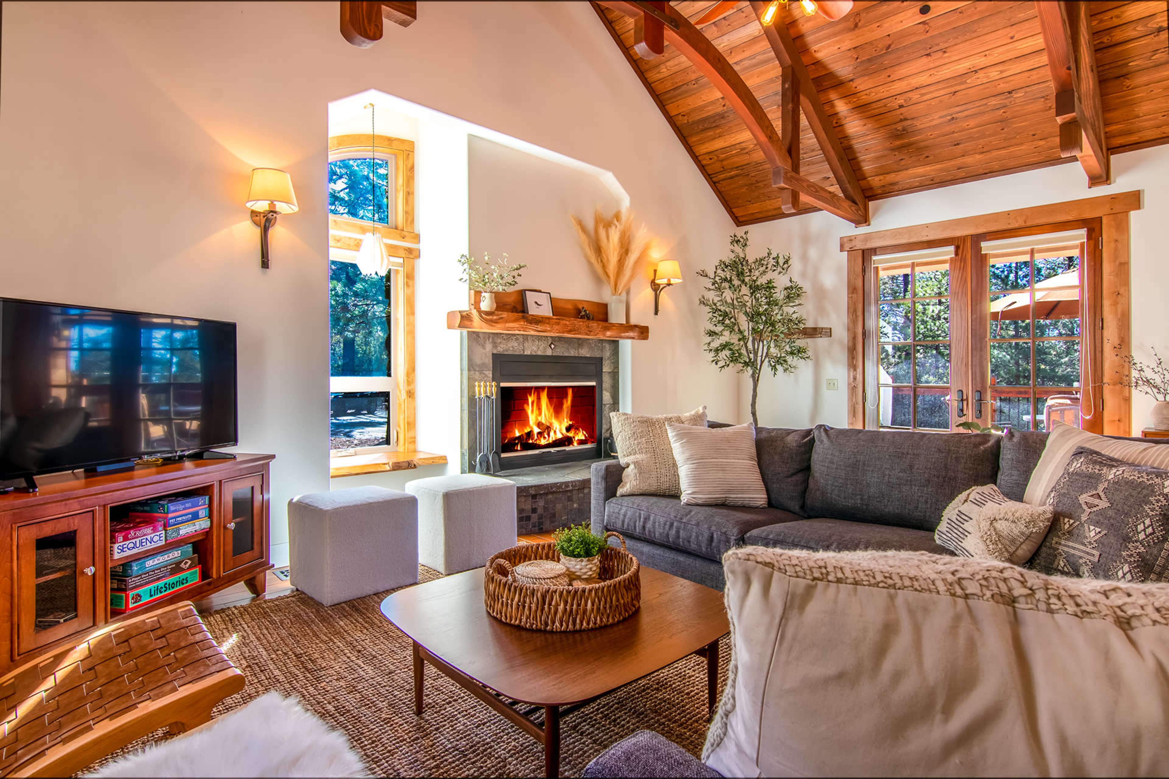 A cozy living room with a fireplace, large windows, and a sectional sofa arranged around a coffee table.