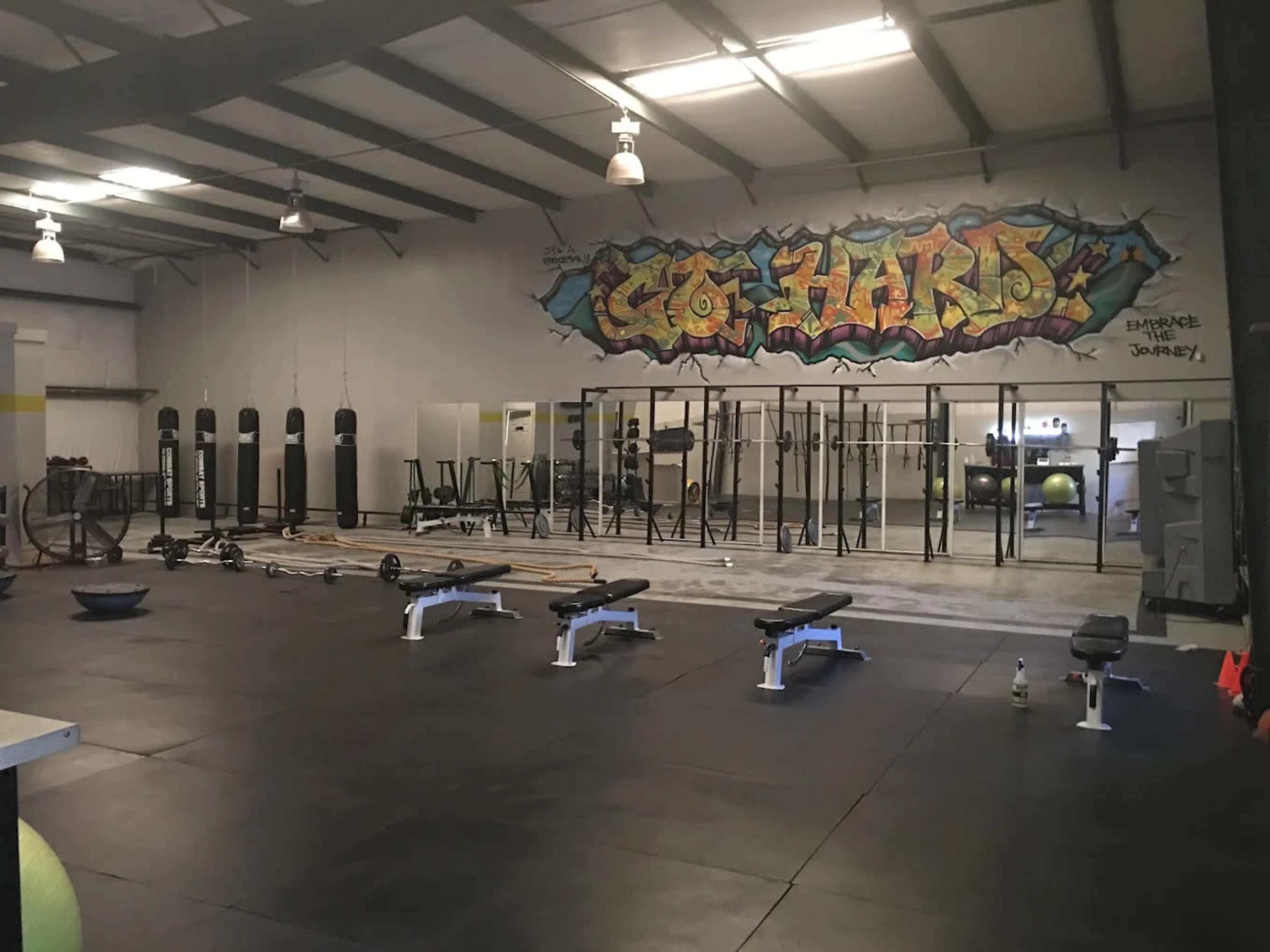 The image shows a spacious gym interior with various workout equipment, including benches, weights, and a wall featuring colorful graffiti art.