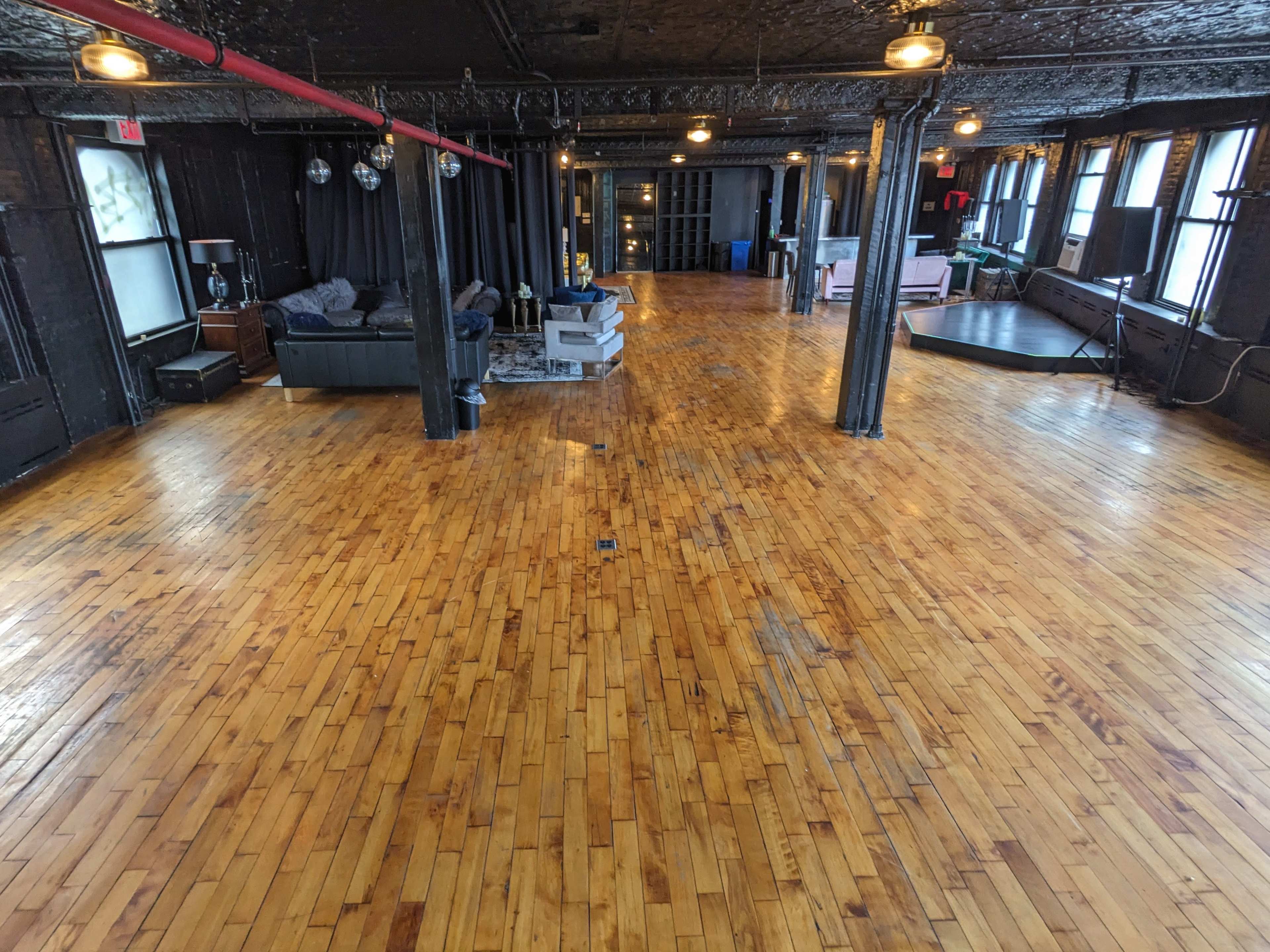 A spacious wooden-floored room with dark walls, large windows, and various seating areas.