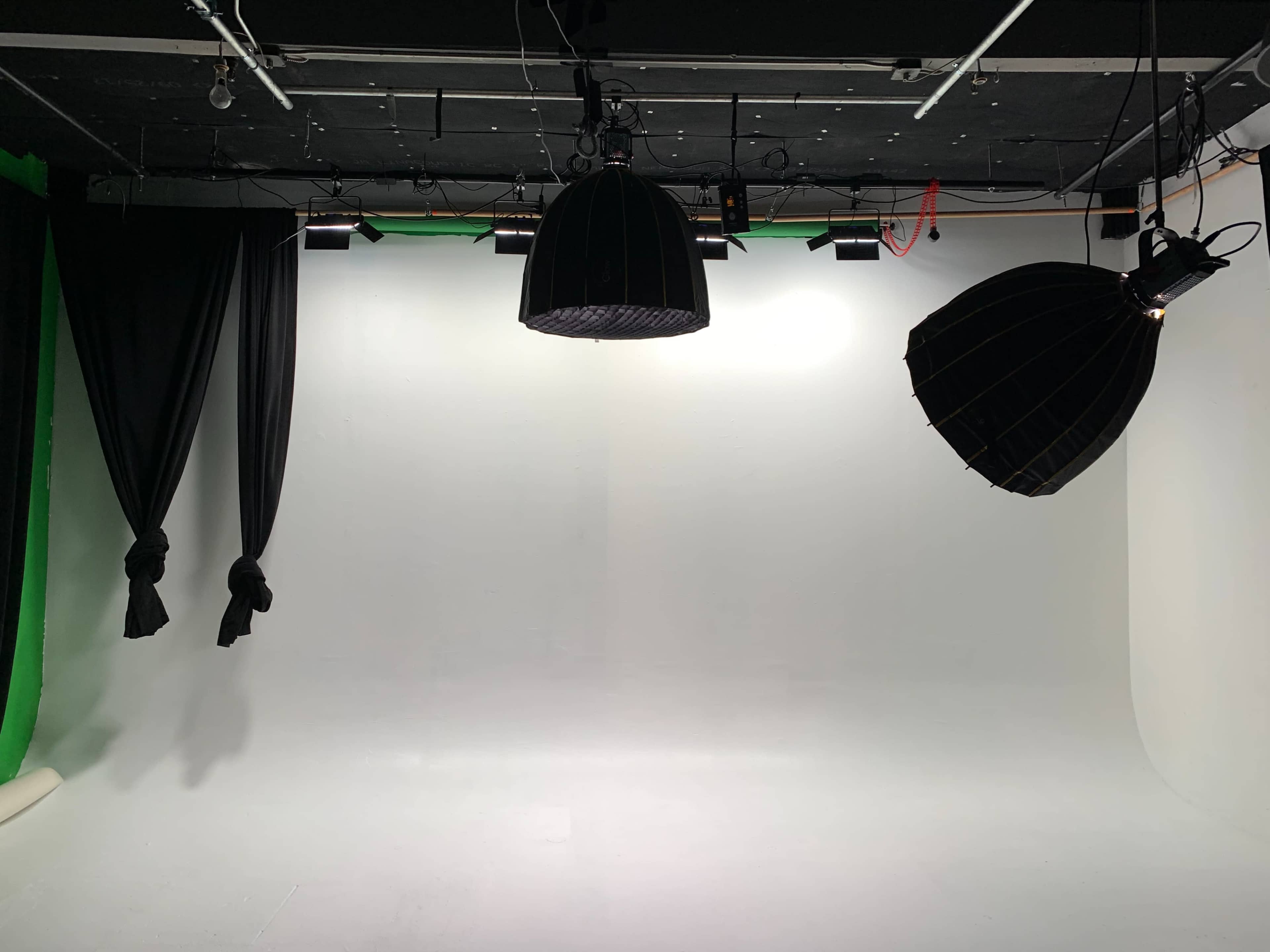 A sparsely furnished photography studio with a white backdrop, two hanging lights, and black curtains.