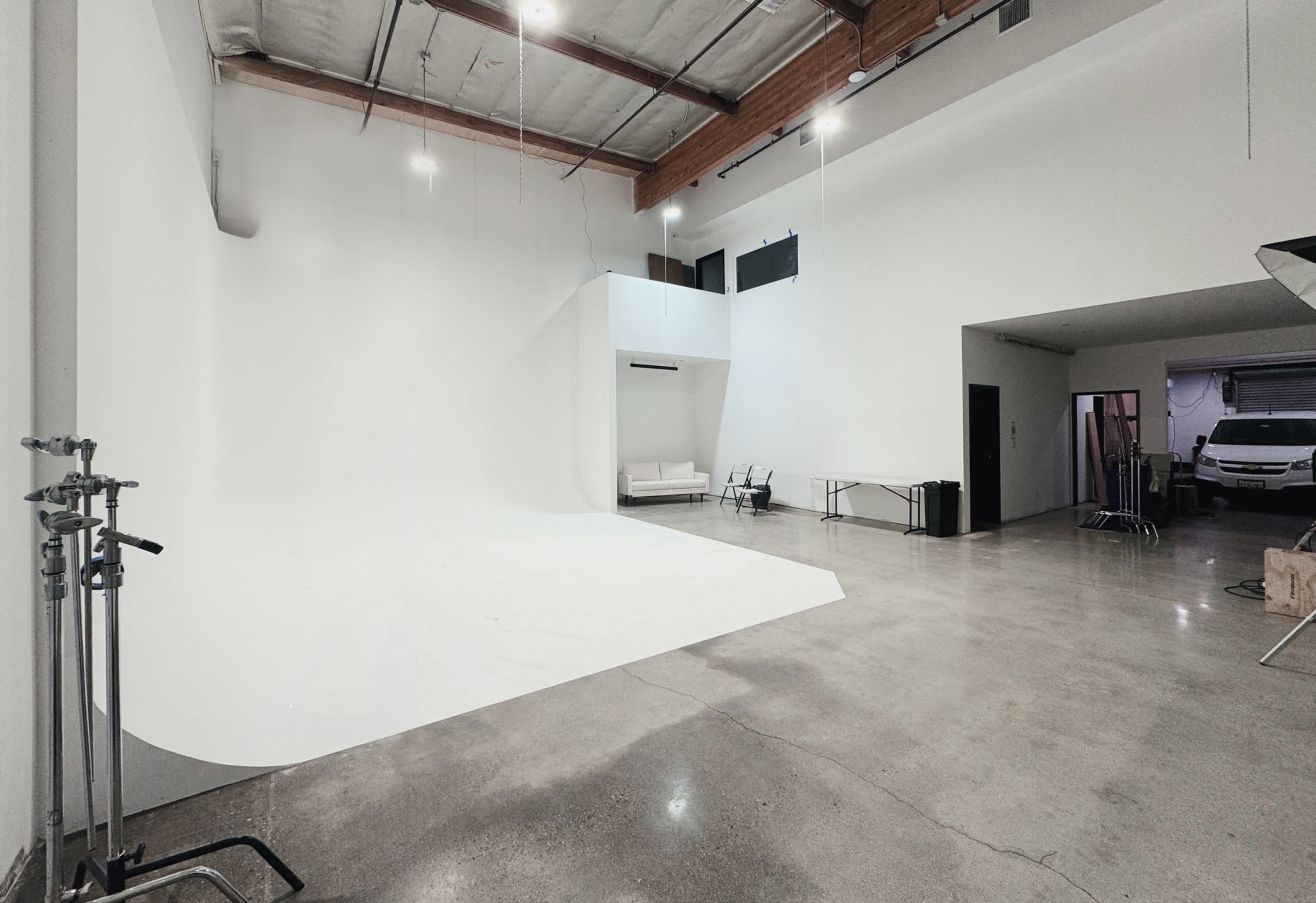The image shows a spacious, empty photo studio with a white backdrop and polished concrete floors.