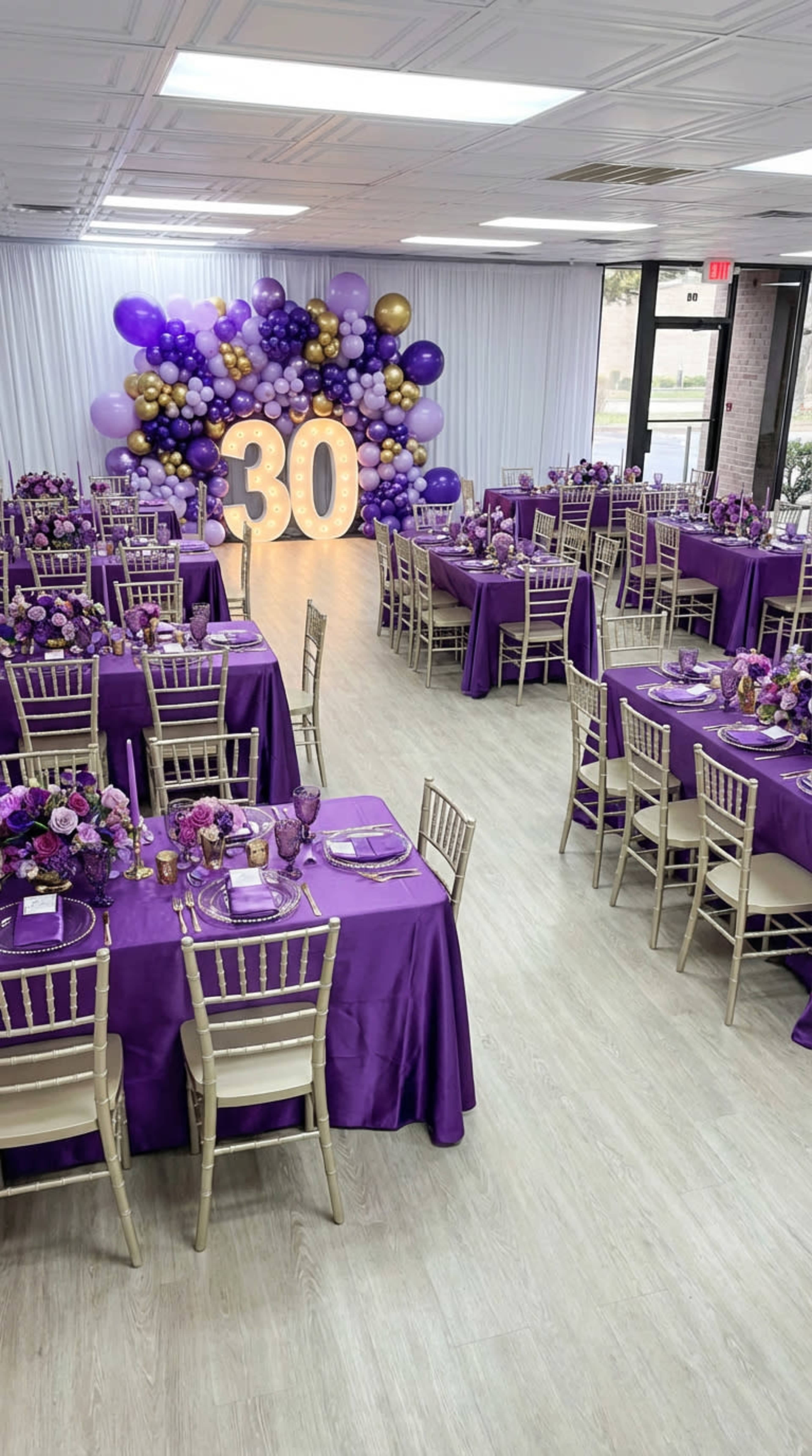 The image shows a banquet hall decorated for a 30th birthday party, featuring purple tablecloths, gold accents, and a balloon arch in the background.