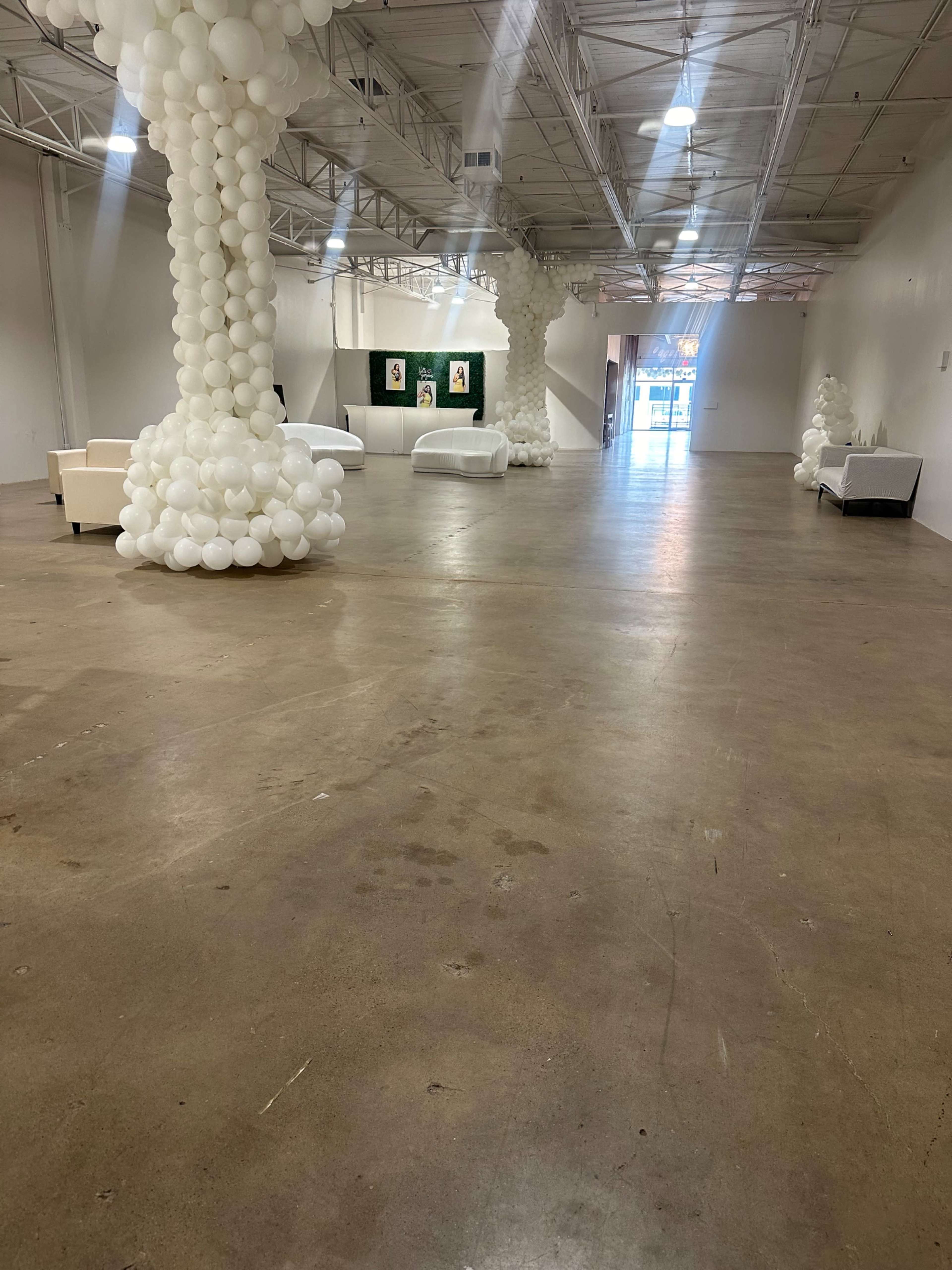 An empty industrial space with white balloon decorations and several white couches arranged throughout.