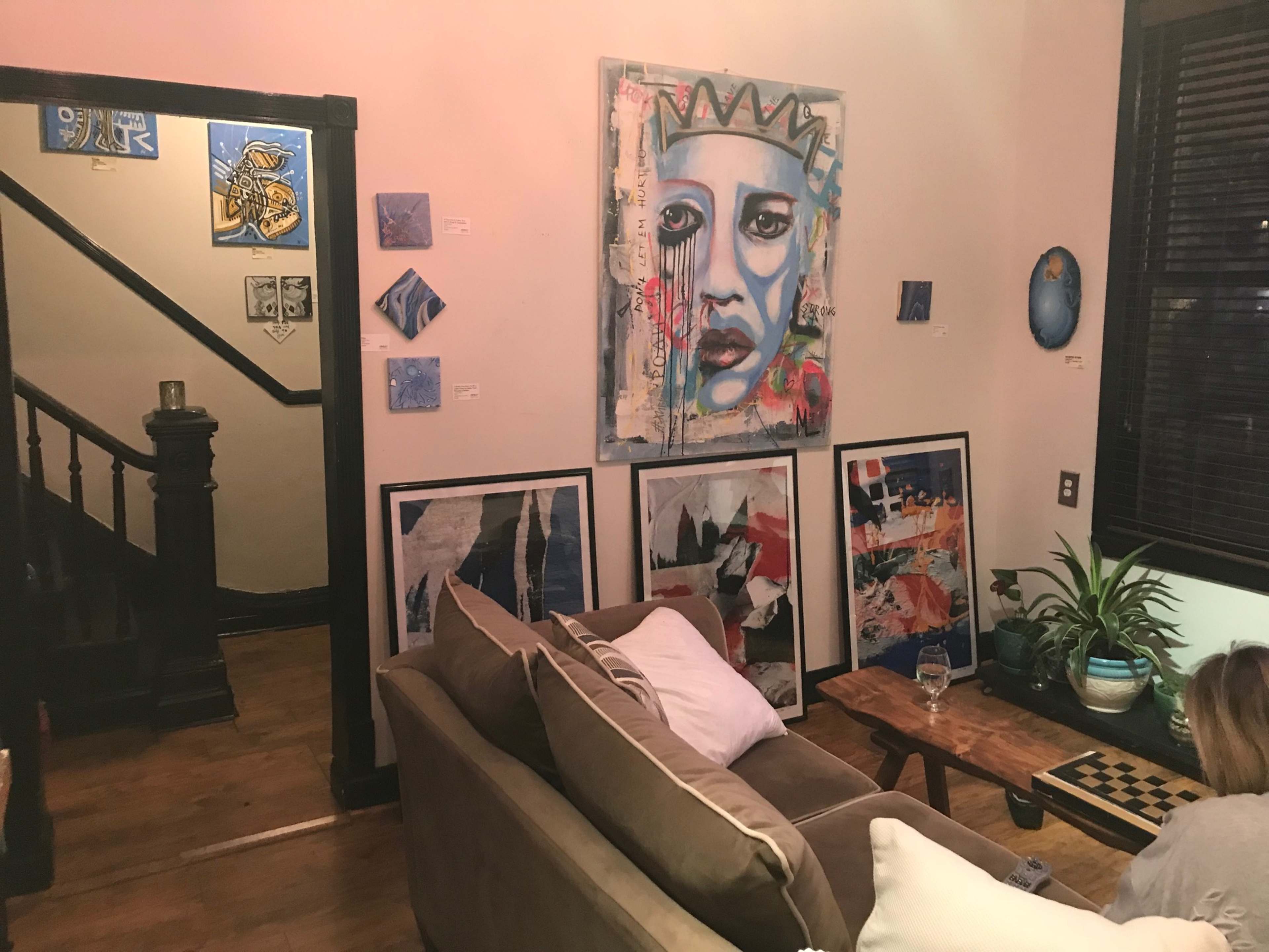 The image depicts a cozy living room with a sofa, a chess board, and several pieces of artwork hanging on the walls, including a large painting of a face.