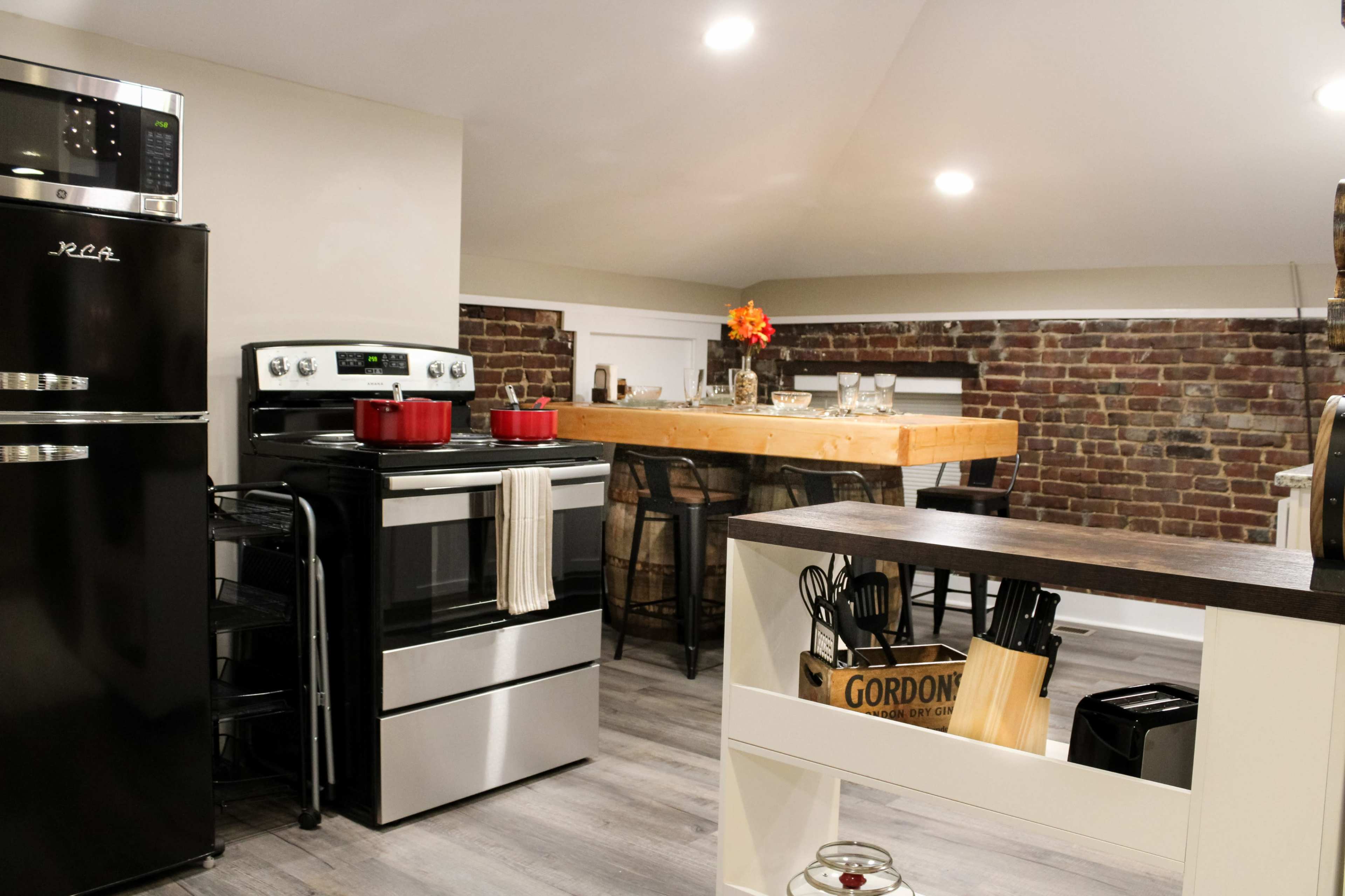 A modern kitchen features stainless steel appliances, a rustic wooden dining table, and exposed brick walls.