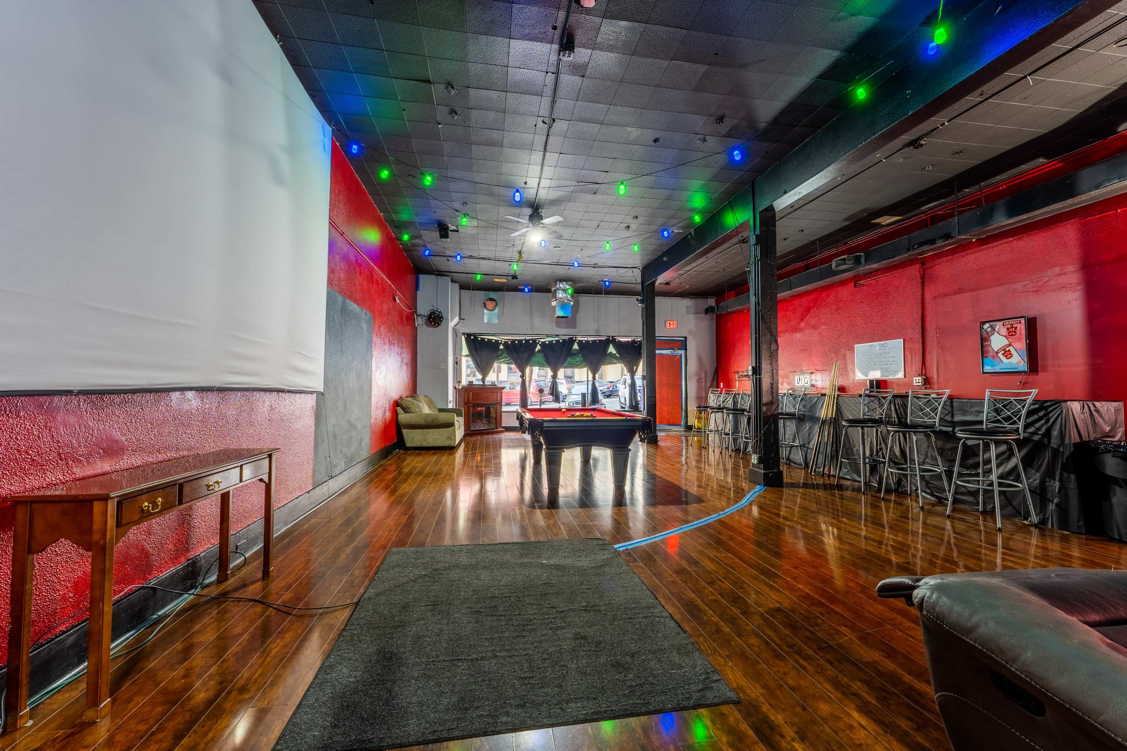 The scene features a spacious room with wooden floors, a pool table, a bar area, and colored lights hanging from the ceiling.